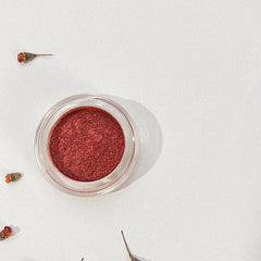 Red powder in clear glass jar with dried flowers on white background
