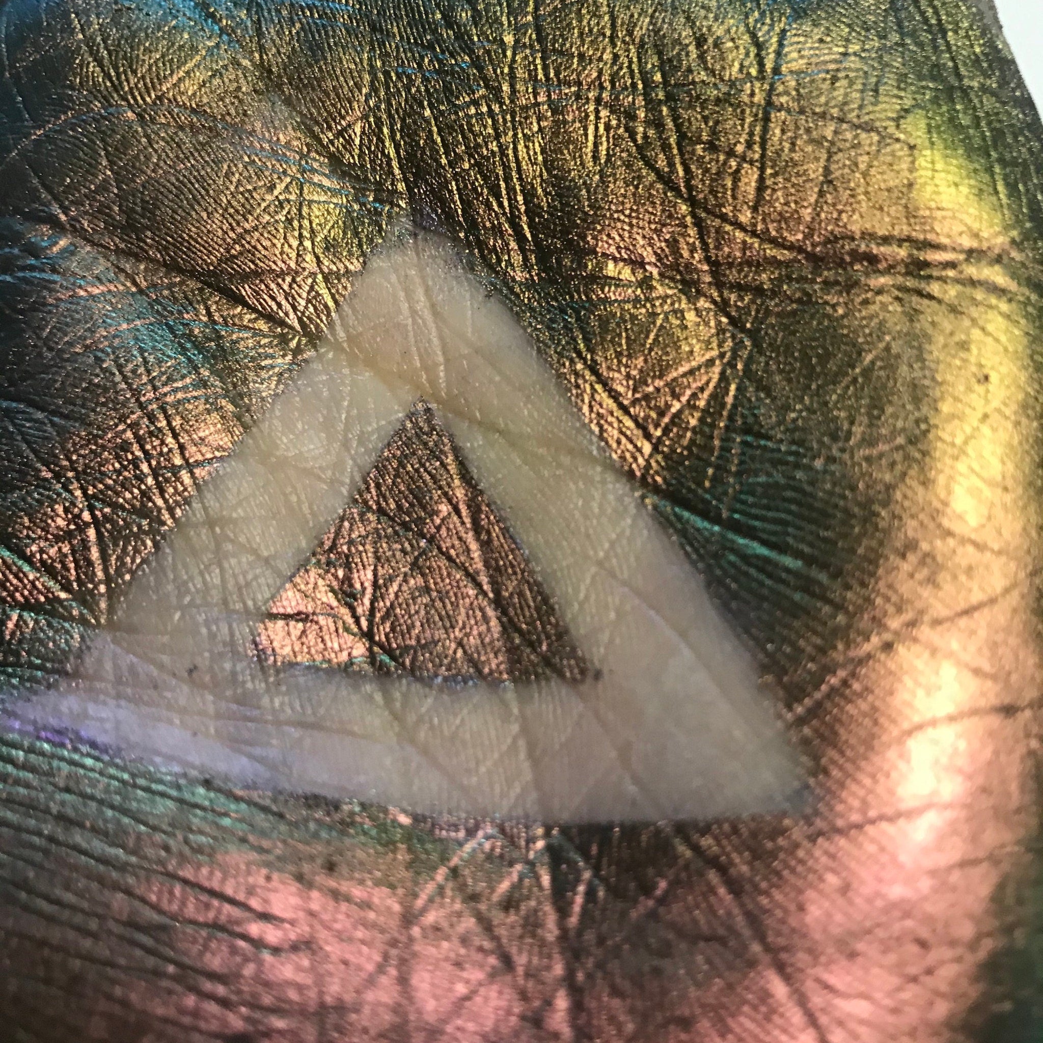 Iridescent textured surface with white triangle, showing green, gold, and pink hues.