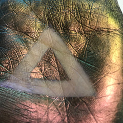 Iridescent textured surface with white triangle, showing green, gold, and pink hues.
