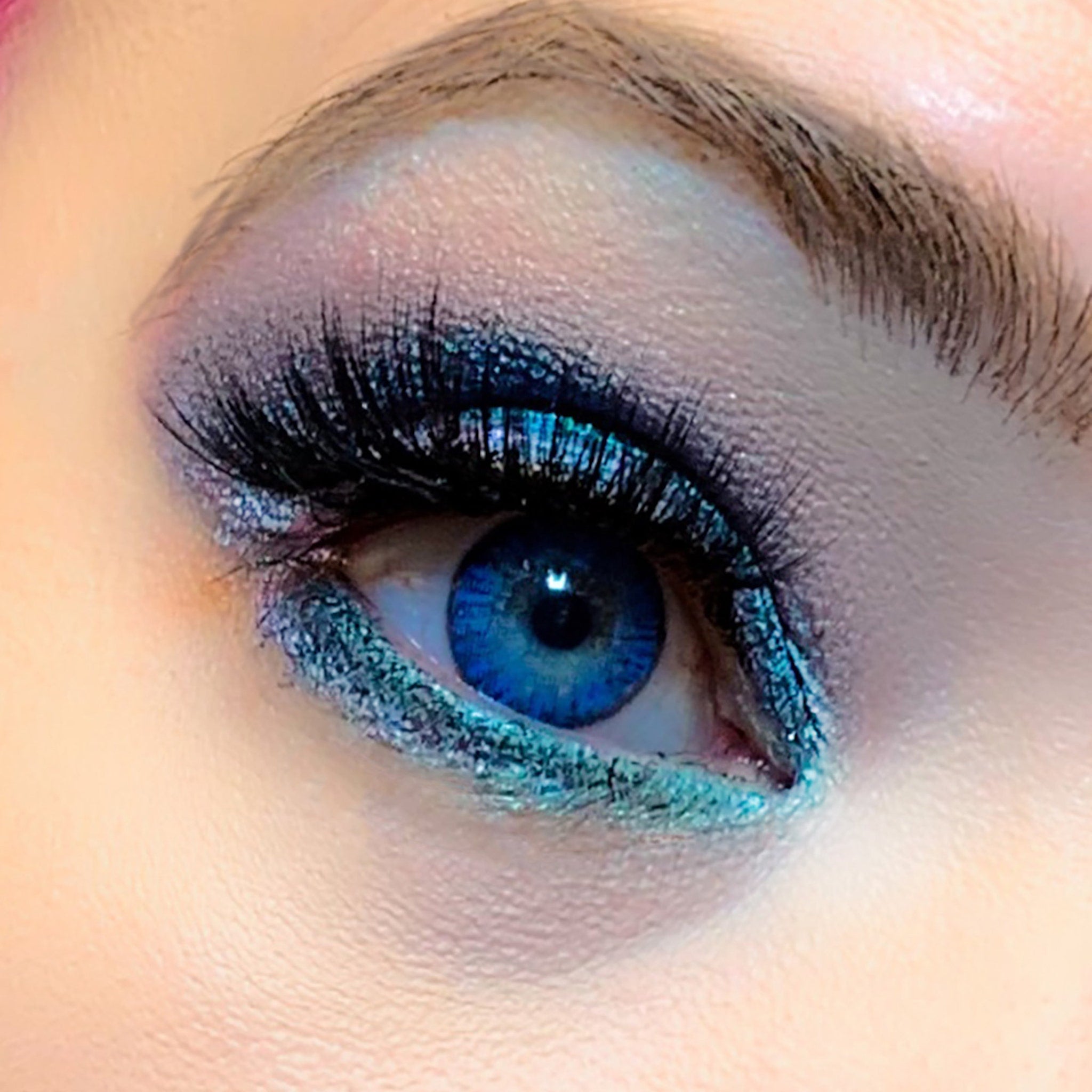 Eye makeup with blue and teal glitter eyeshadow and long black lashes on an eye