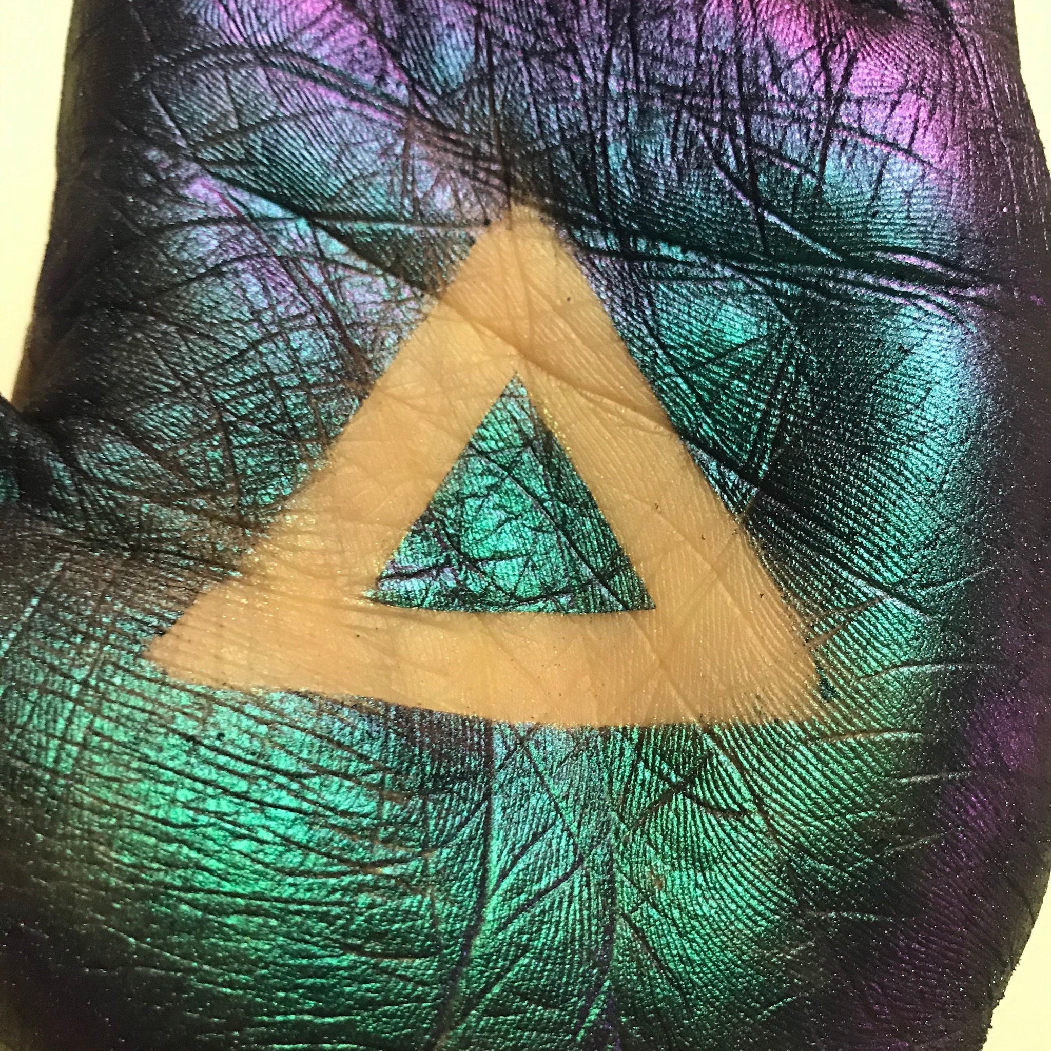 Iridescent textured surface with teal, purple, and yellow triangle shape on hand