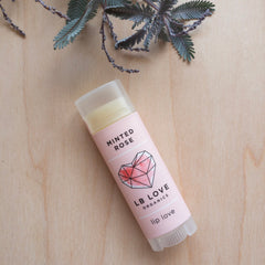 Lip balm tube with pink label, geometric heart, and LB LOVE ORGANICS text on wood surface