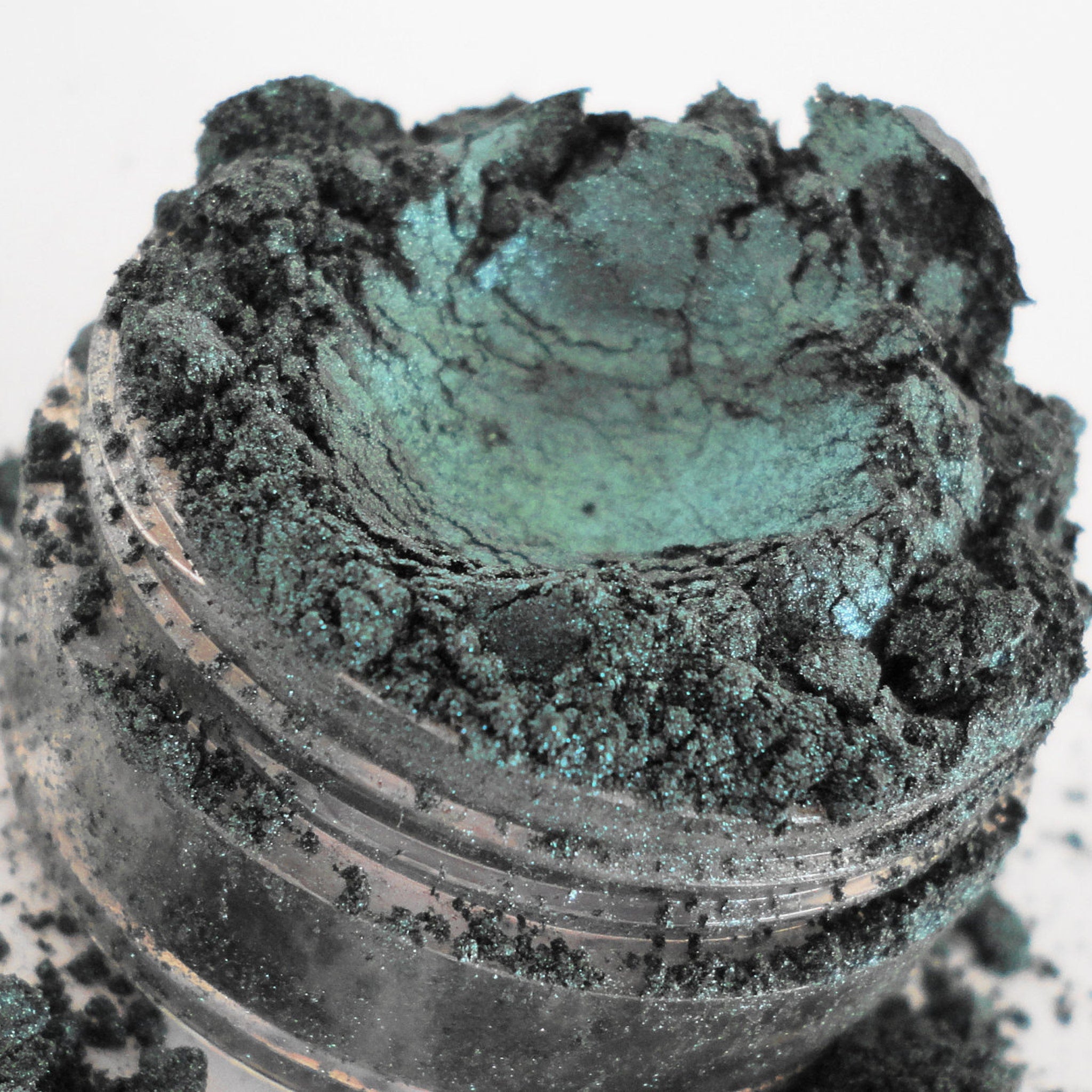 Side view of teal green metallic eyeshadow pot showing shimmer luster and sifter lid details