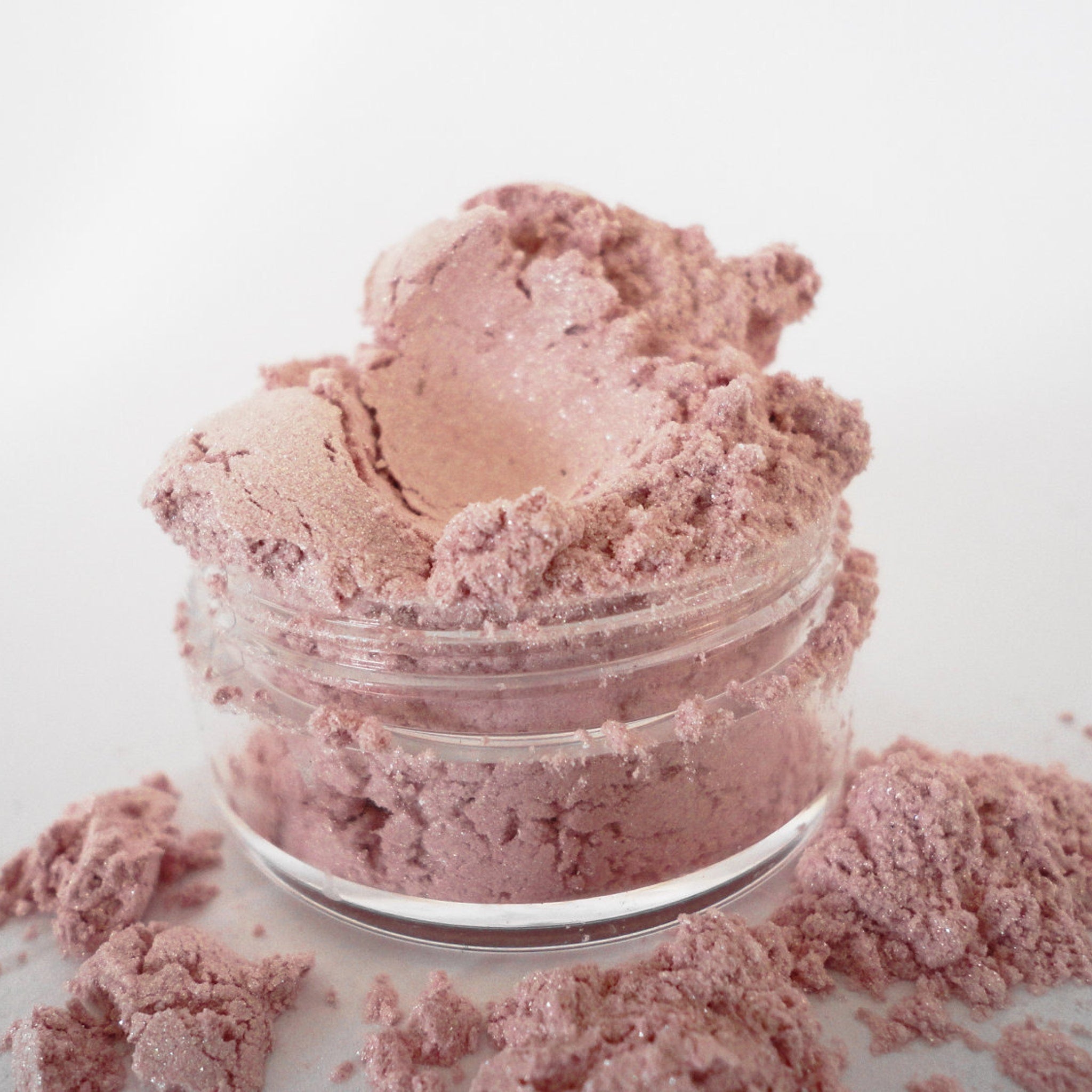Woman applying pink coral shimmer eye shadow with fingertip, showcasing natural glitter finish from sifter jar