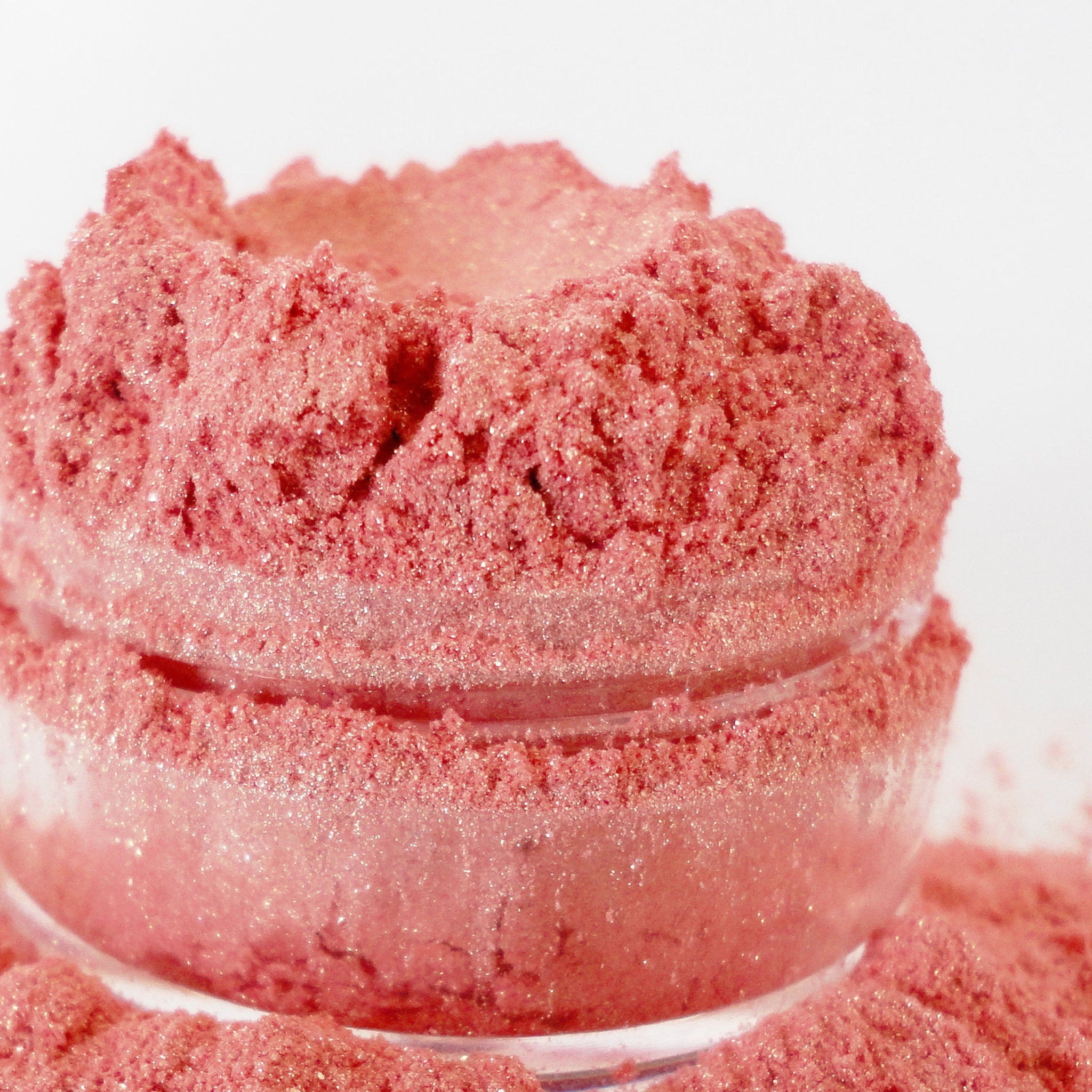 Pink glitter powder in a glass jar, with a shimmering, textured appearance and loose powder around it