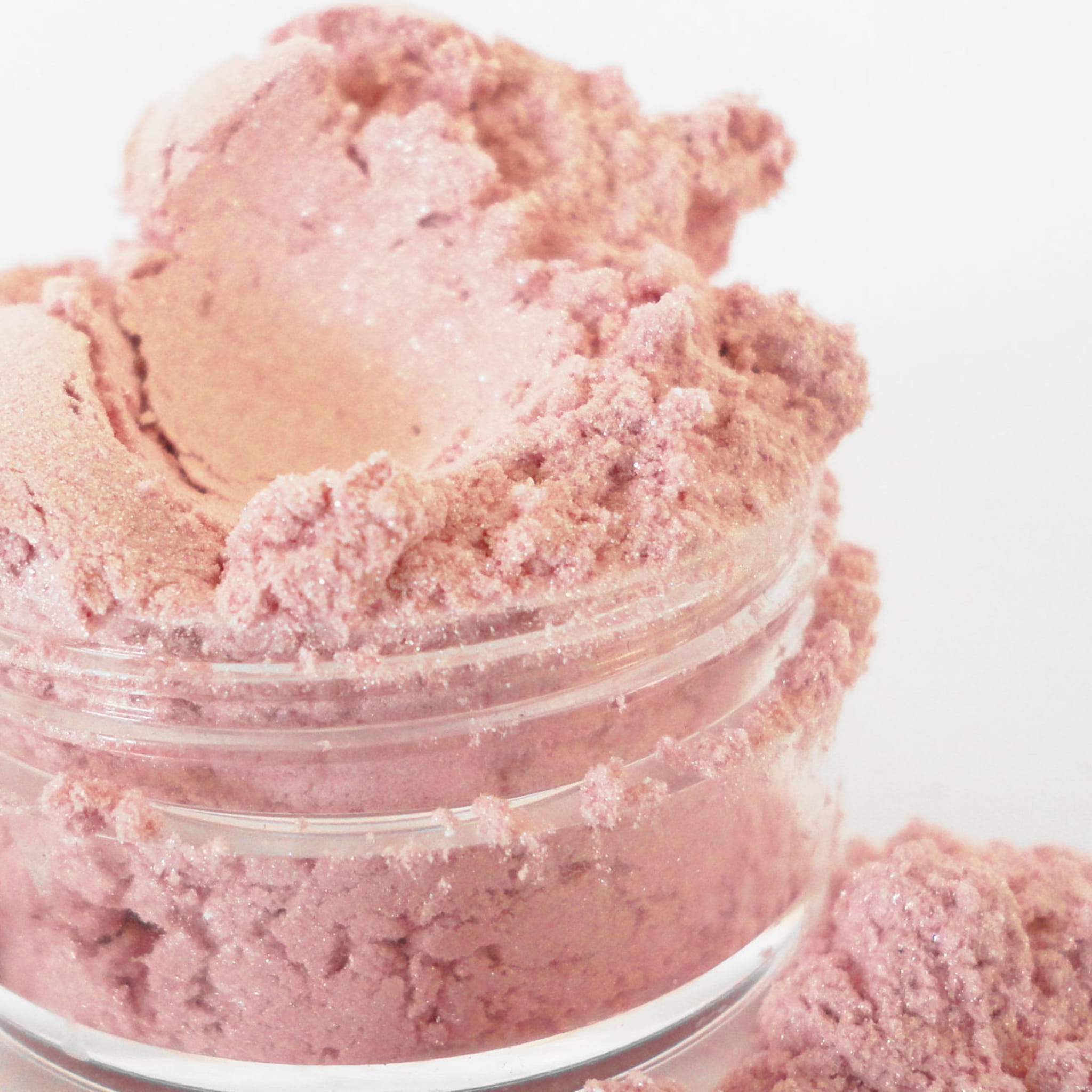 Pink powder makeup in a glass jar, with glitter and a granular texture