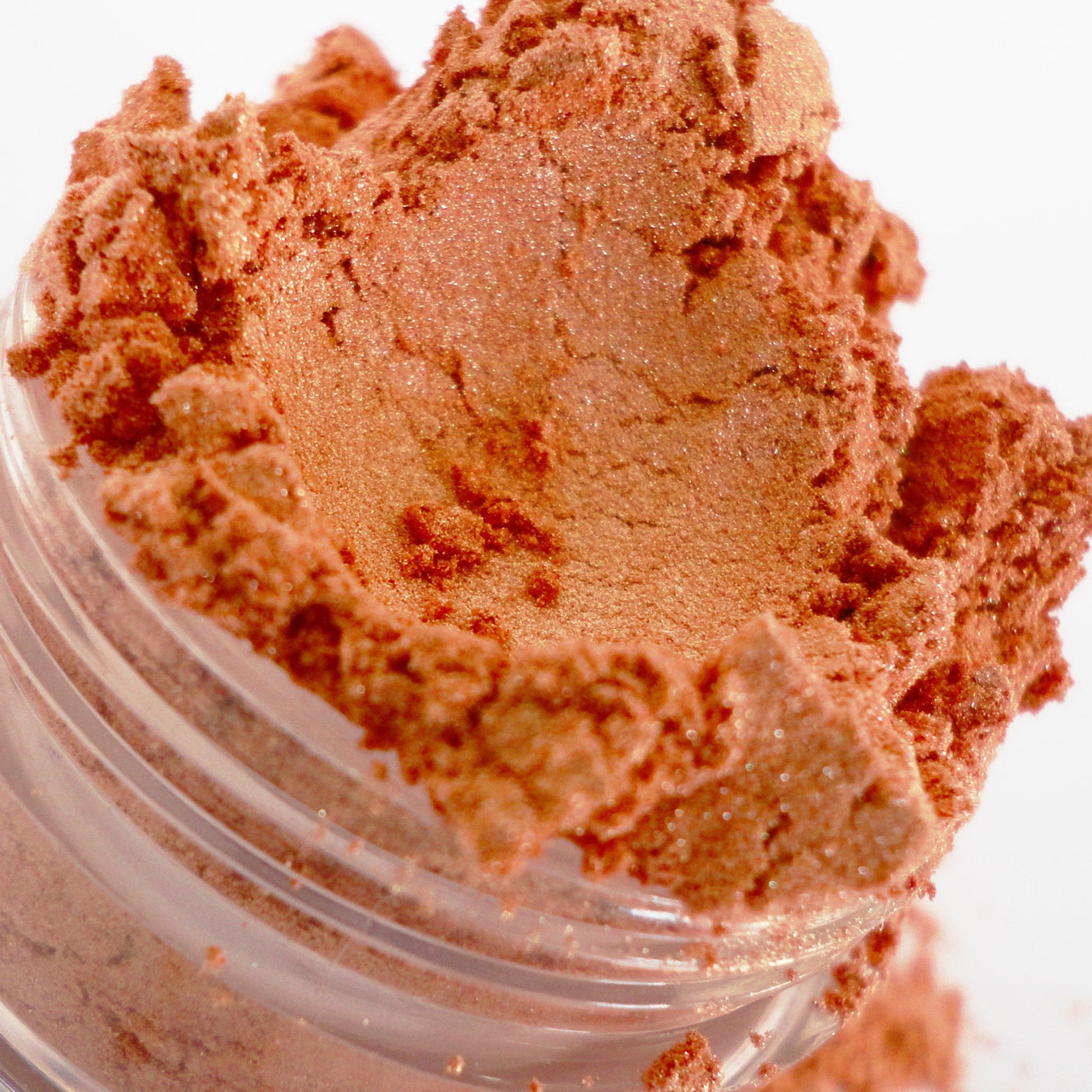Side view of peach shimmer eyeshadow in round jar showing glitter particles catching light