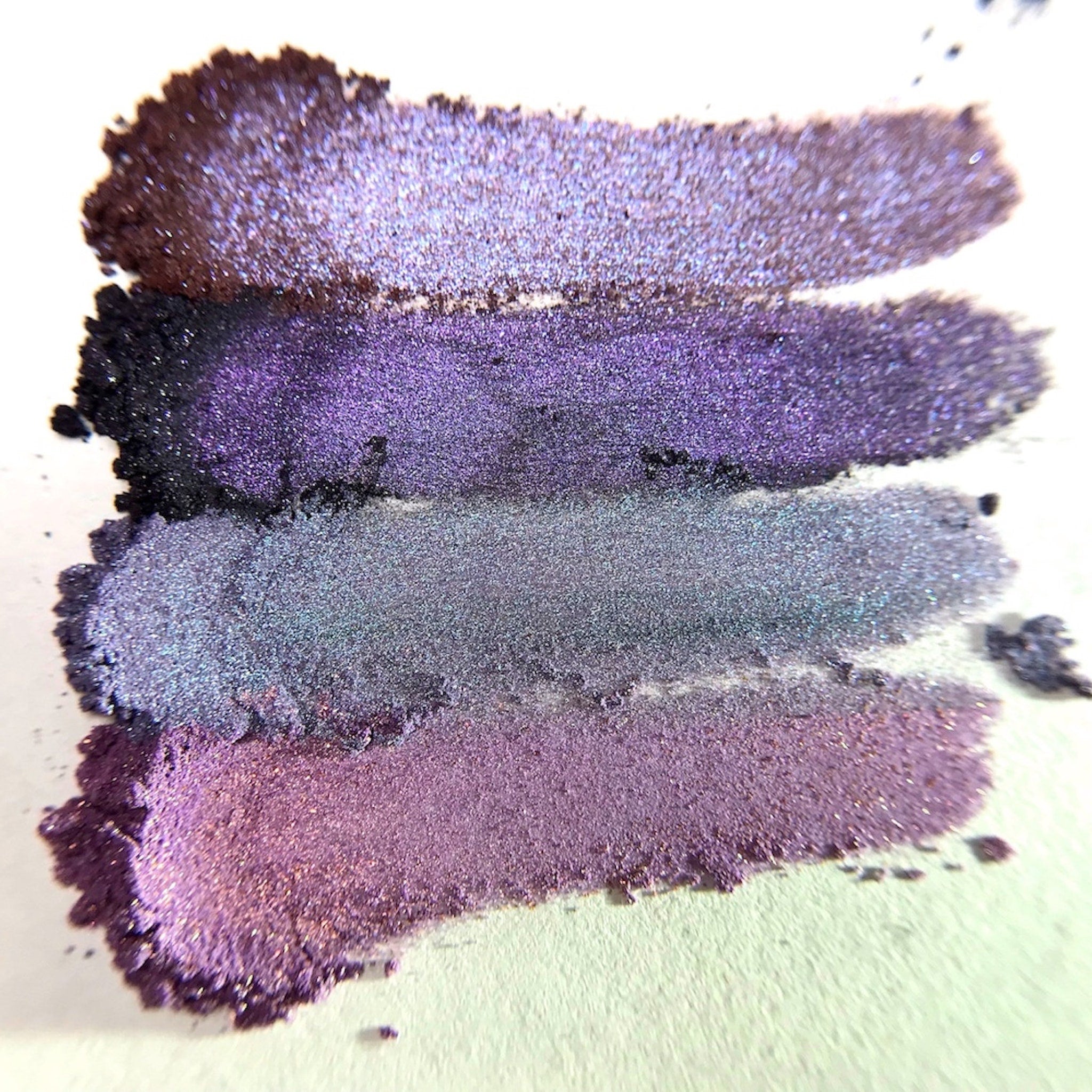 Close-up of fingertips applying black mineral eyeshadow with smooth, velvety texture to eyelid crease.