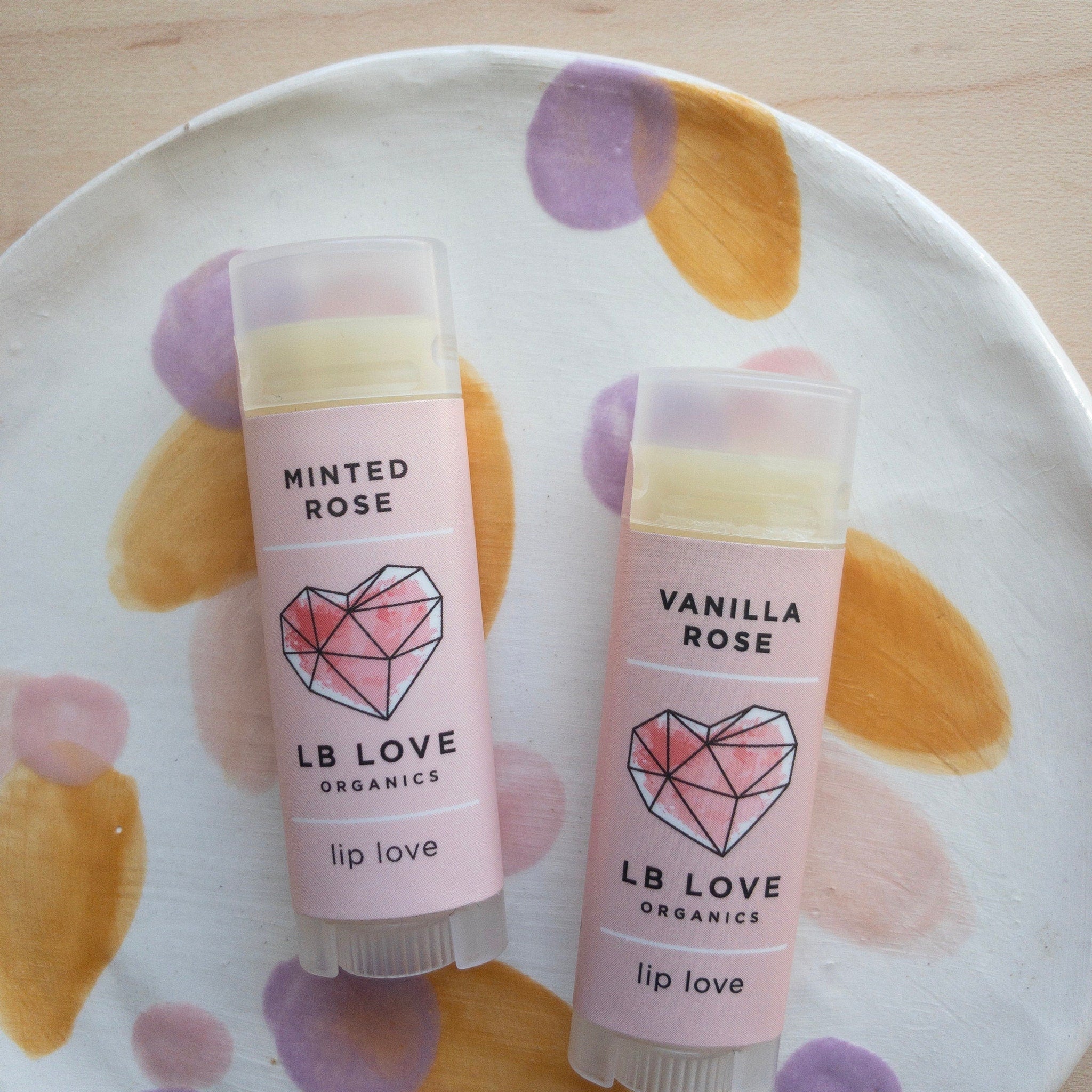 Lip balm tubes with pink labels, clear caps, and LB Love branding on a decorative plate