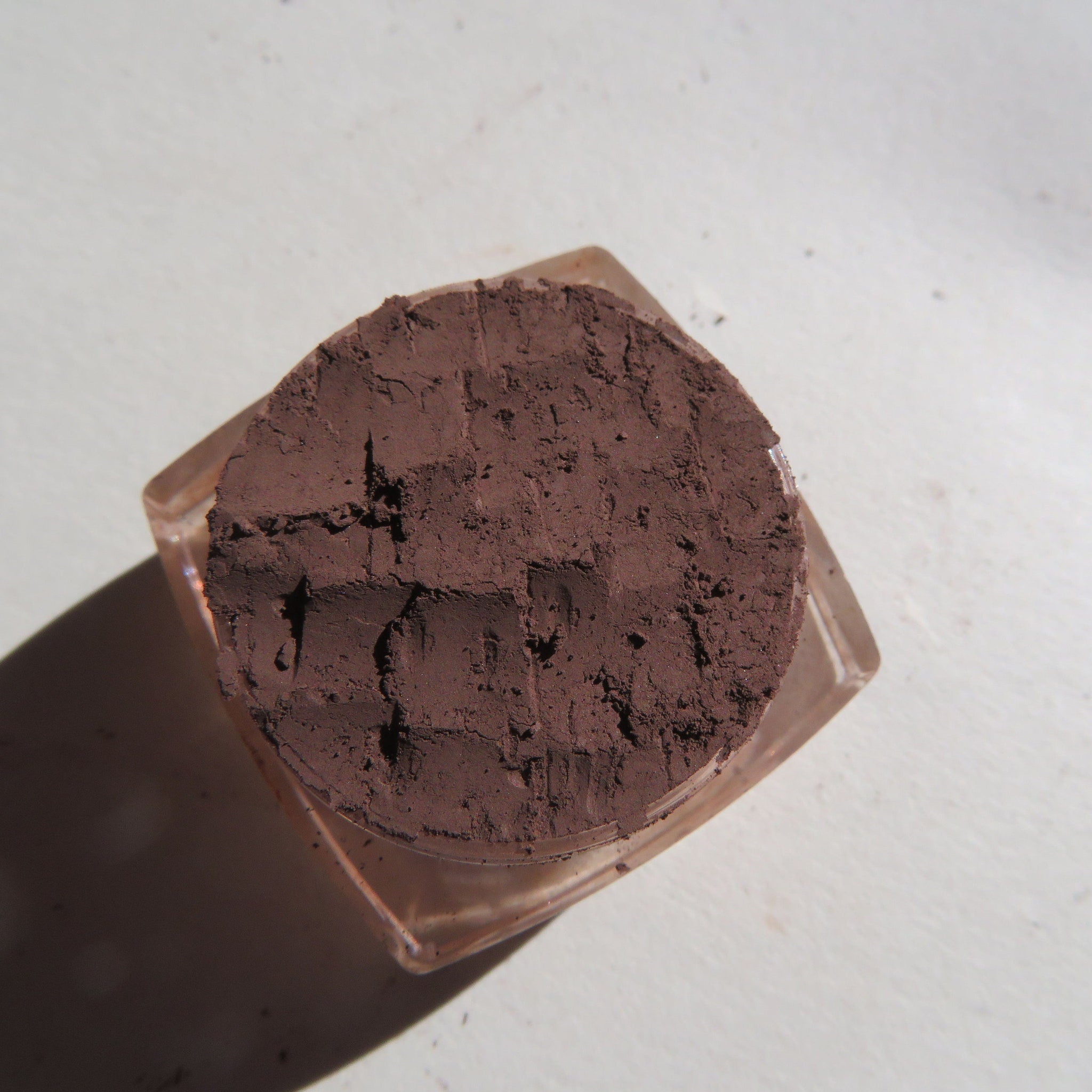 Brown powder in a clear glass container with a textured surface on a white background