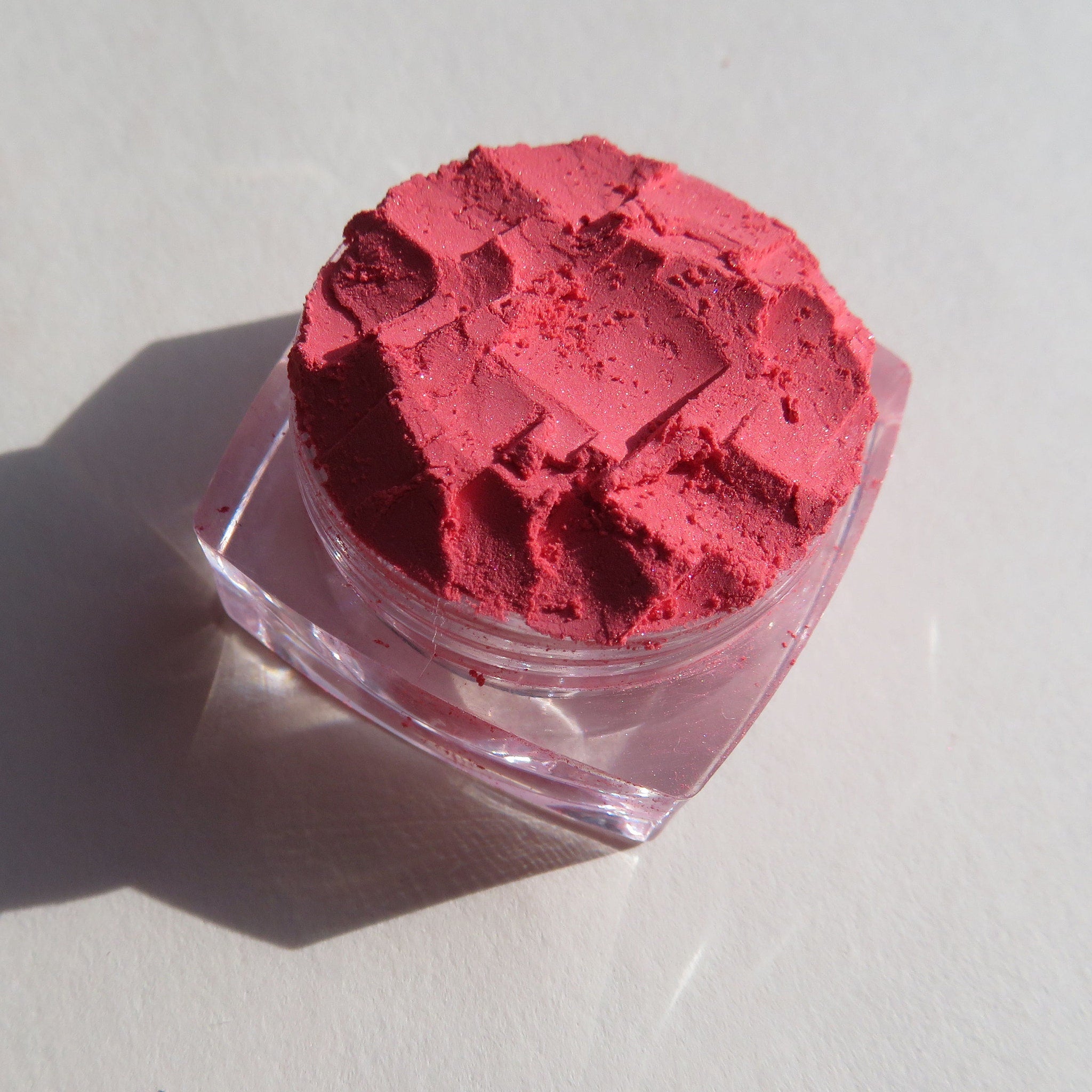 Close-up of matte coral pink loose mineral eyeshadow with soft powdery texture in a vegan, talc-free formula.