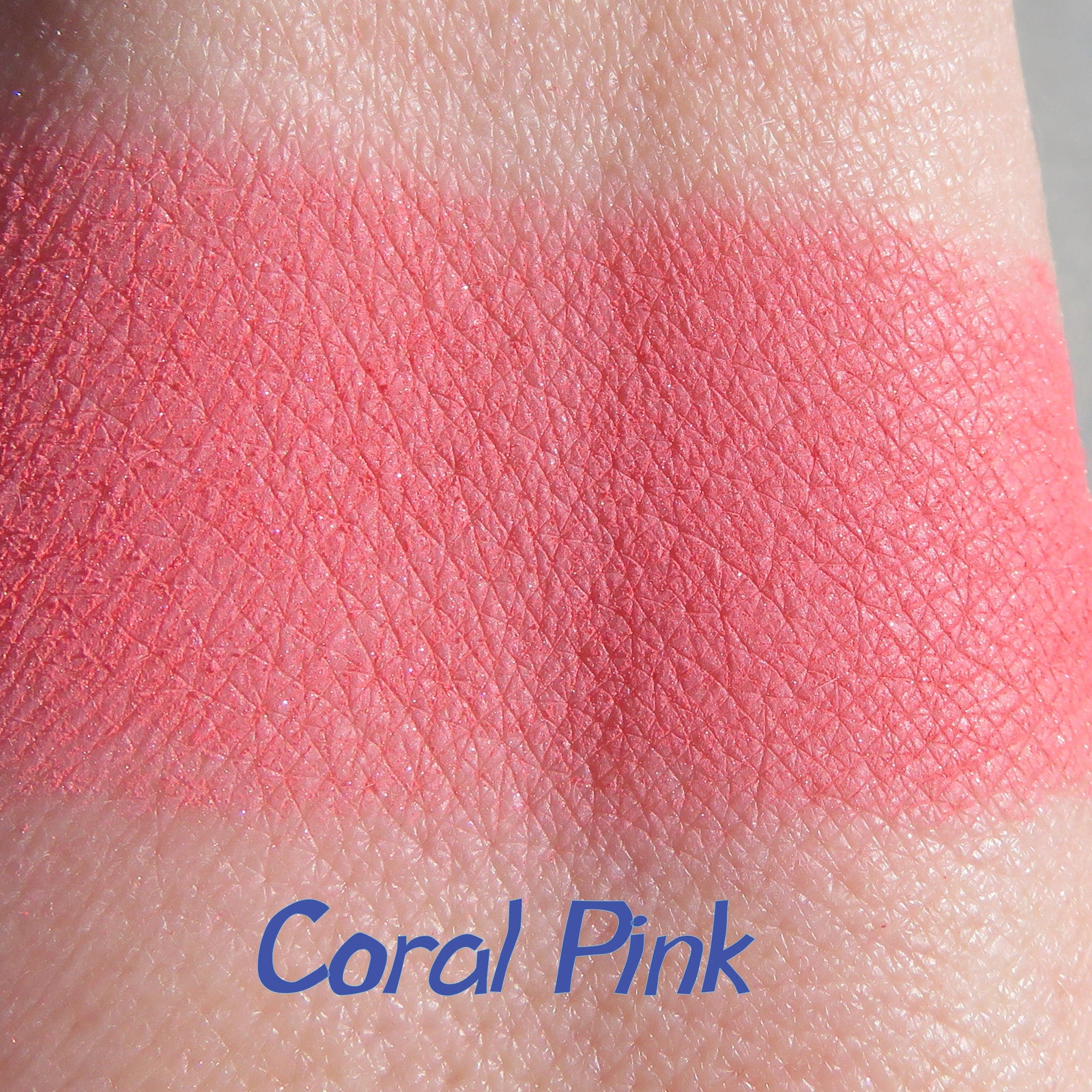 Side view of loose matte coral pink mineral eyeshadow powder spilling from jar onto surface