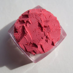 Hand applying matte coral pink mineral eyeshadow with fingertip onto eyelid, showing loose pigment texture