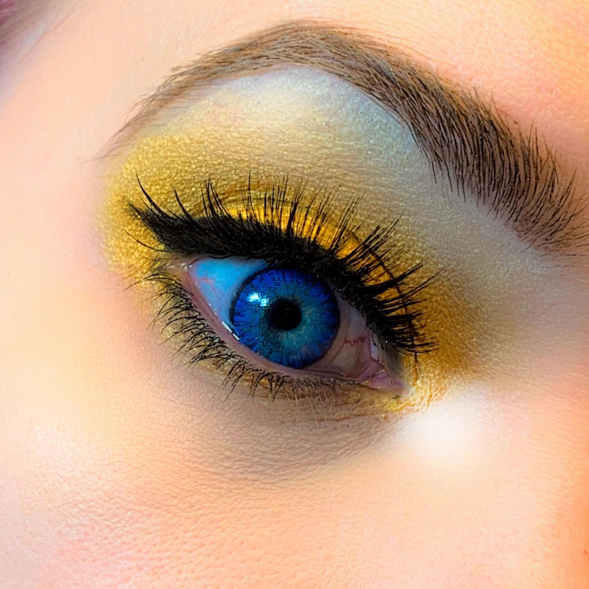 Blue eye with gold eyeshadow and black eyelashes, close-up view of eye makeup