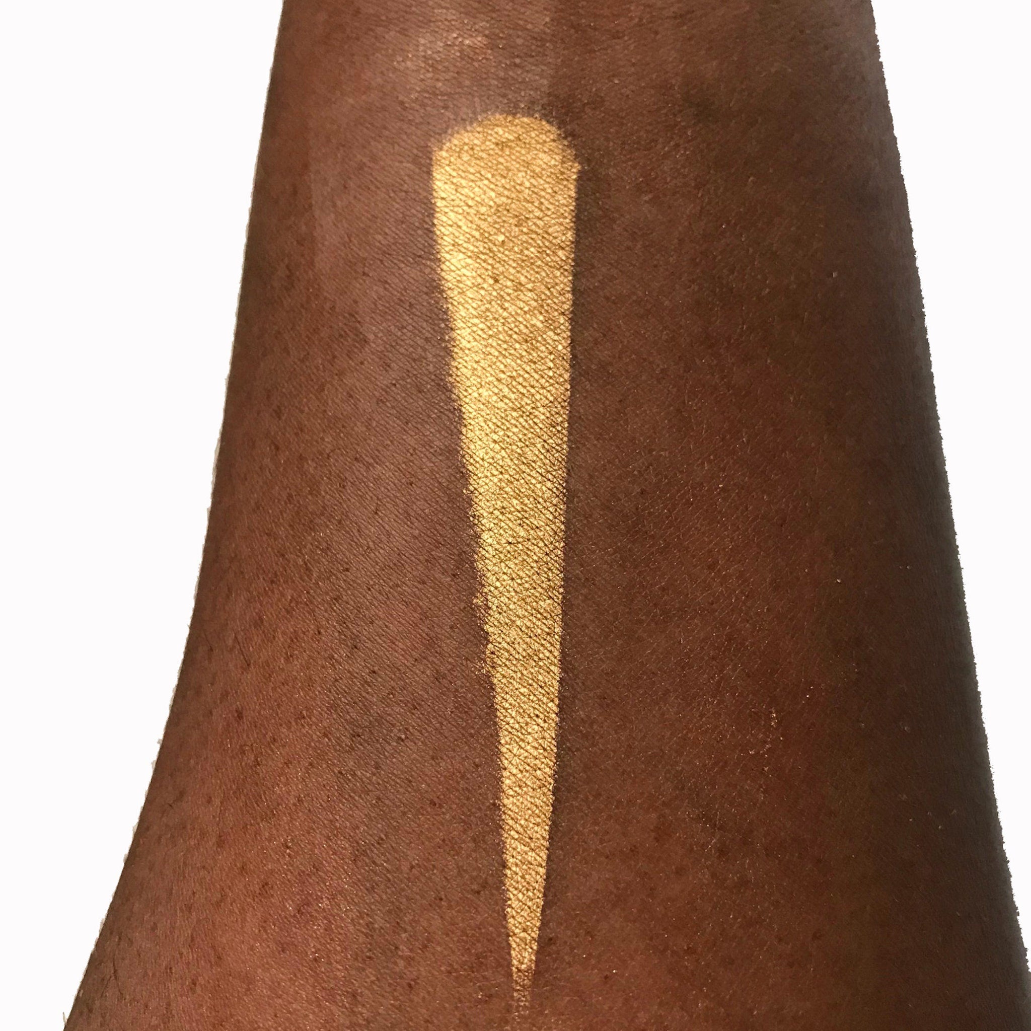 Close-up of fingertips applying shimmery bronze halo eyeshadow to eyelid with smooth metallic finish