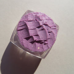 Purple eyeshadow with glitter, textured surface, in clear container