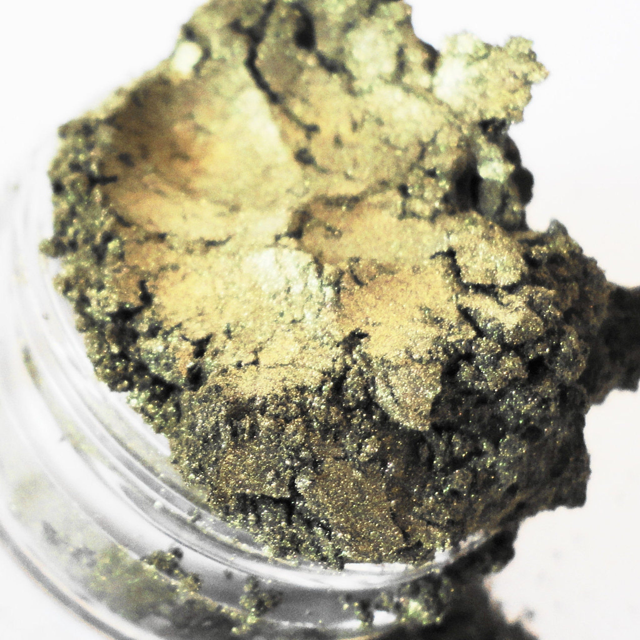 Eye shadow powder, golden green, textured, in a clear jar, close-up view