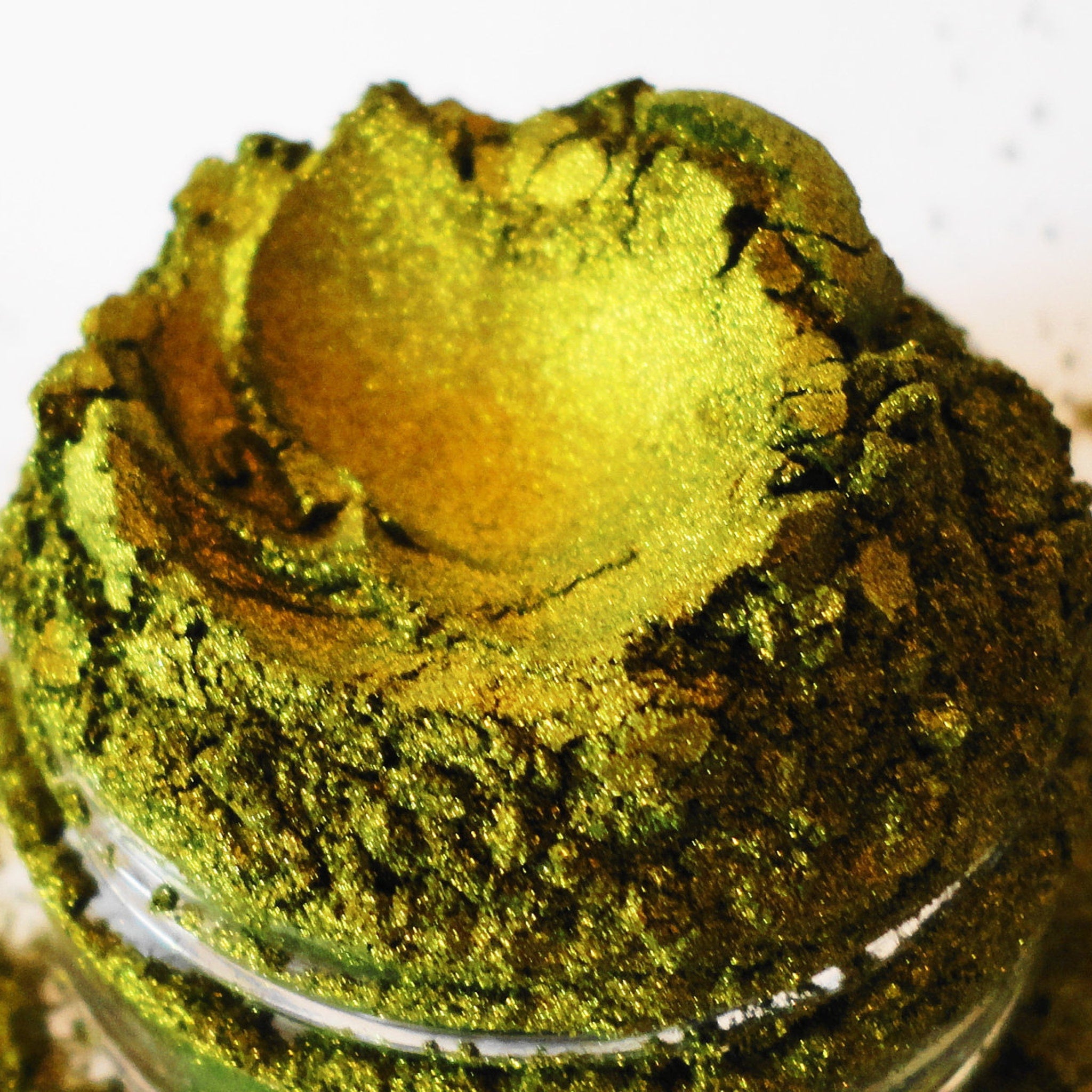 Green and gold powder with textured appearance in a clear glass container