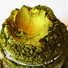 Green and gold powder with textured appearance in a clear glass container