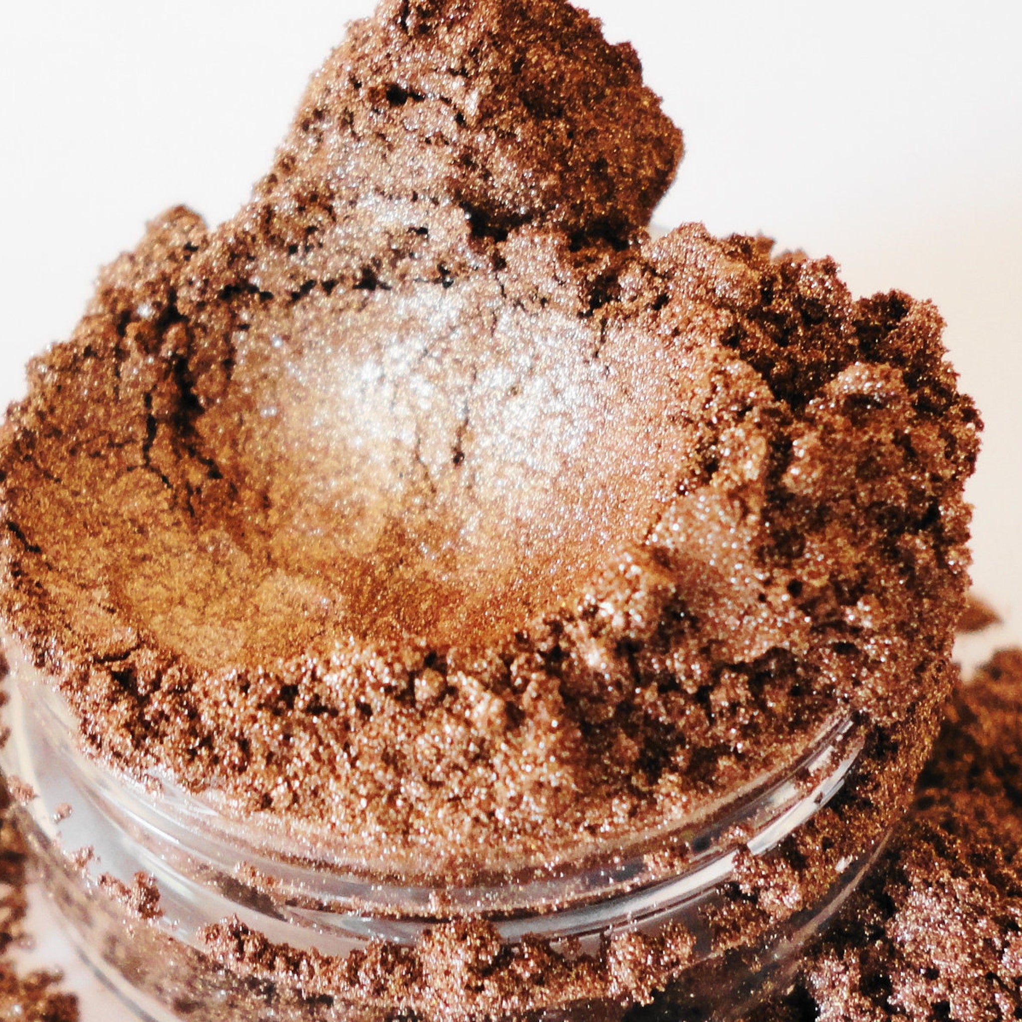 Eye shadow powder, brown metallic shimmer, in a clear glass jar, close-up view