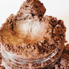 Brown eyeshadow powder with shimmer, in a clear glass jar, close-up view