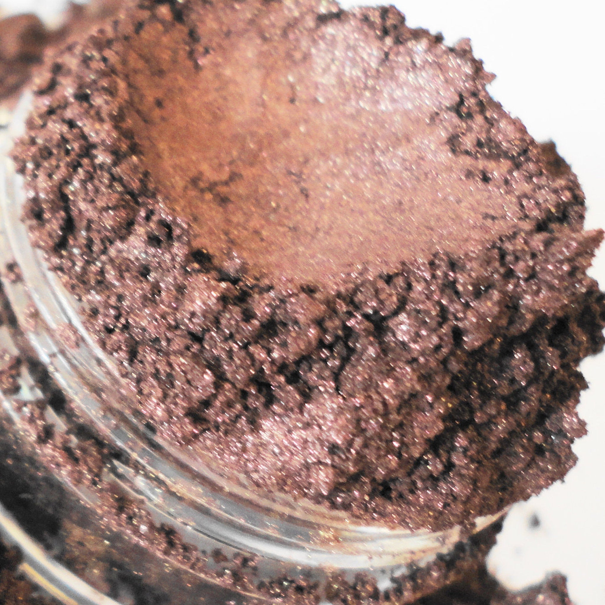 Eye shadow, brown metallic powder in a clear glass jar, close-up view