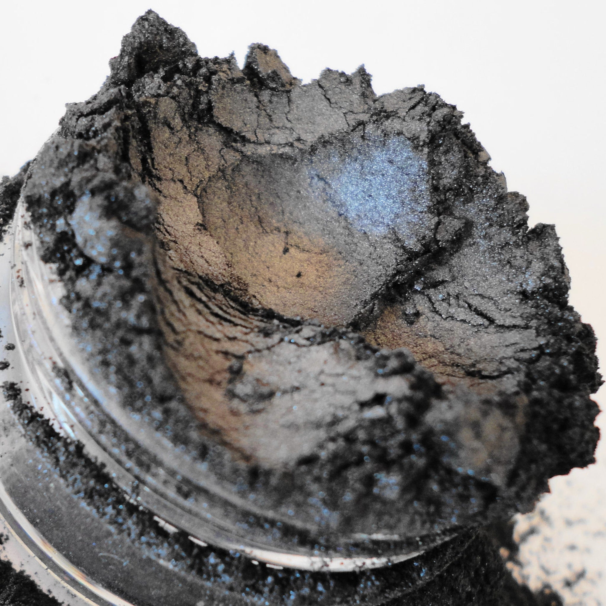 Black eyeshadow powder with metallic shimmer and chunky texture in a jar