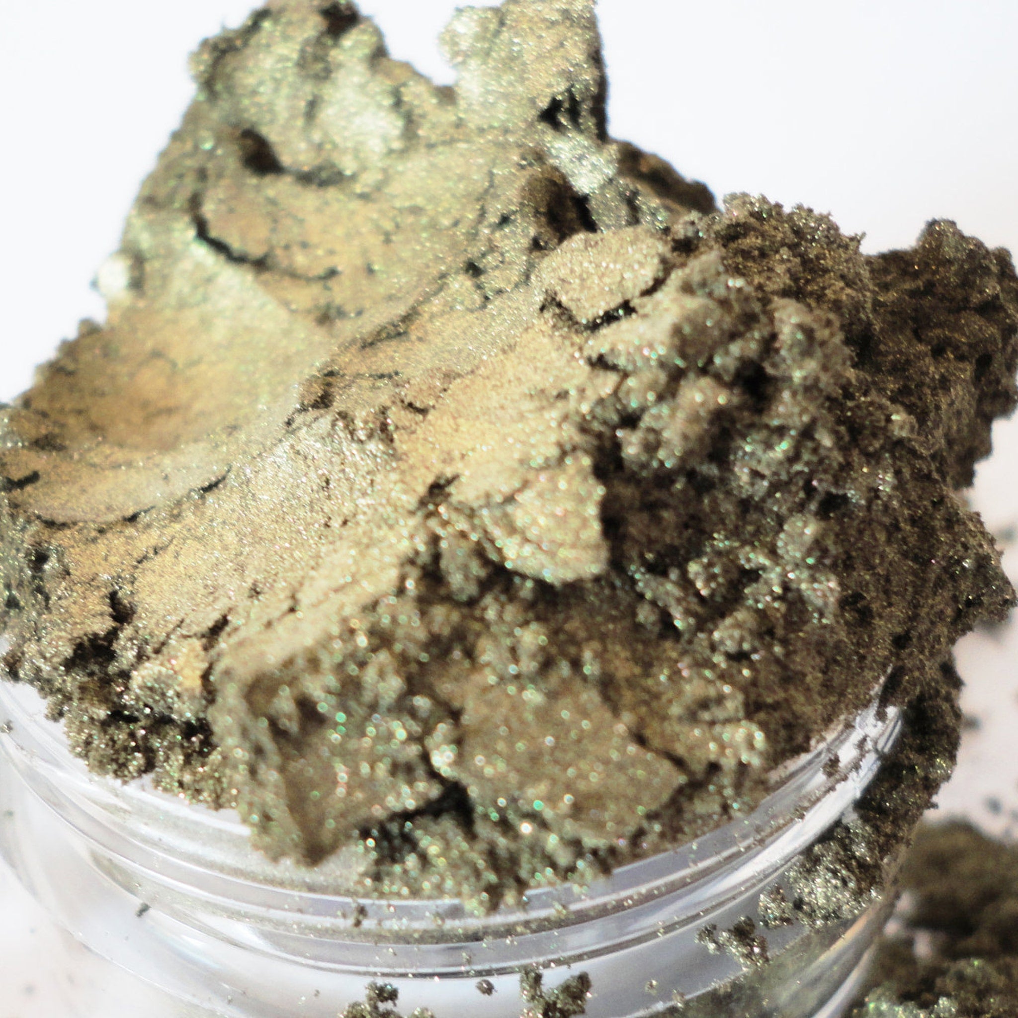 Eyeshadow powder in metallic green and gold with glittery texture, in a clear container