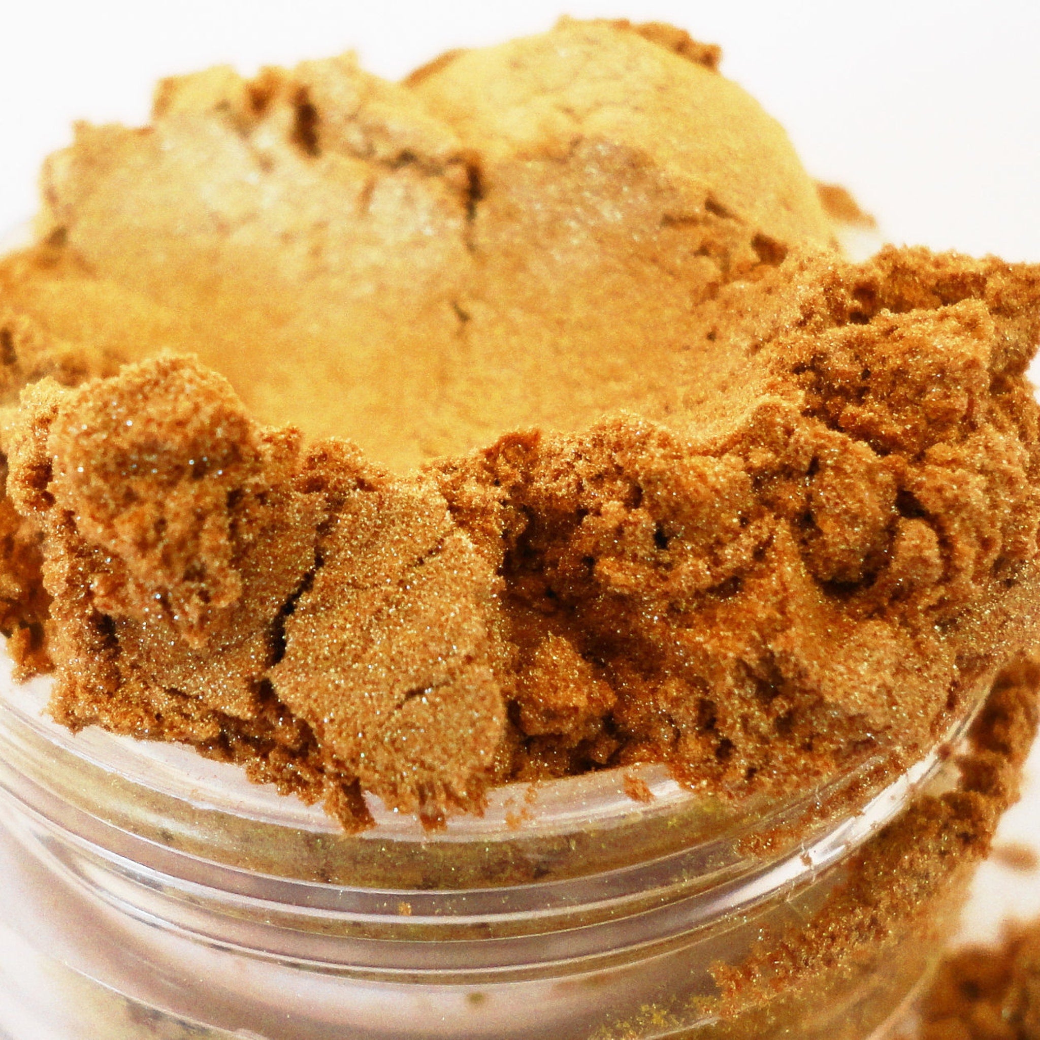 Gold eyeshadow, sparkling bronze powder, in clear jar, close-up view
