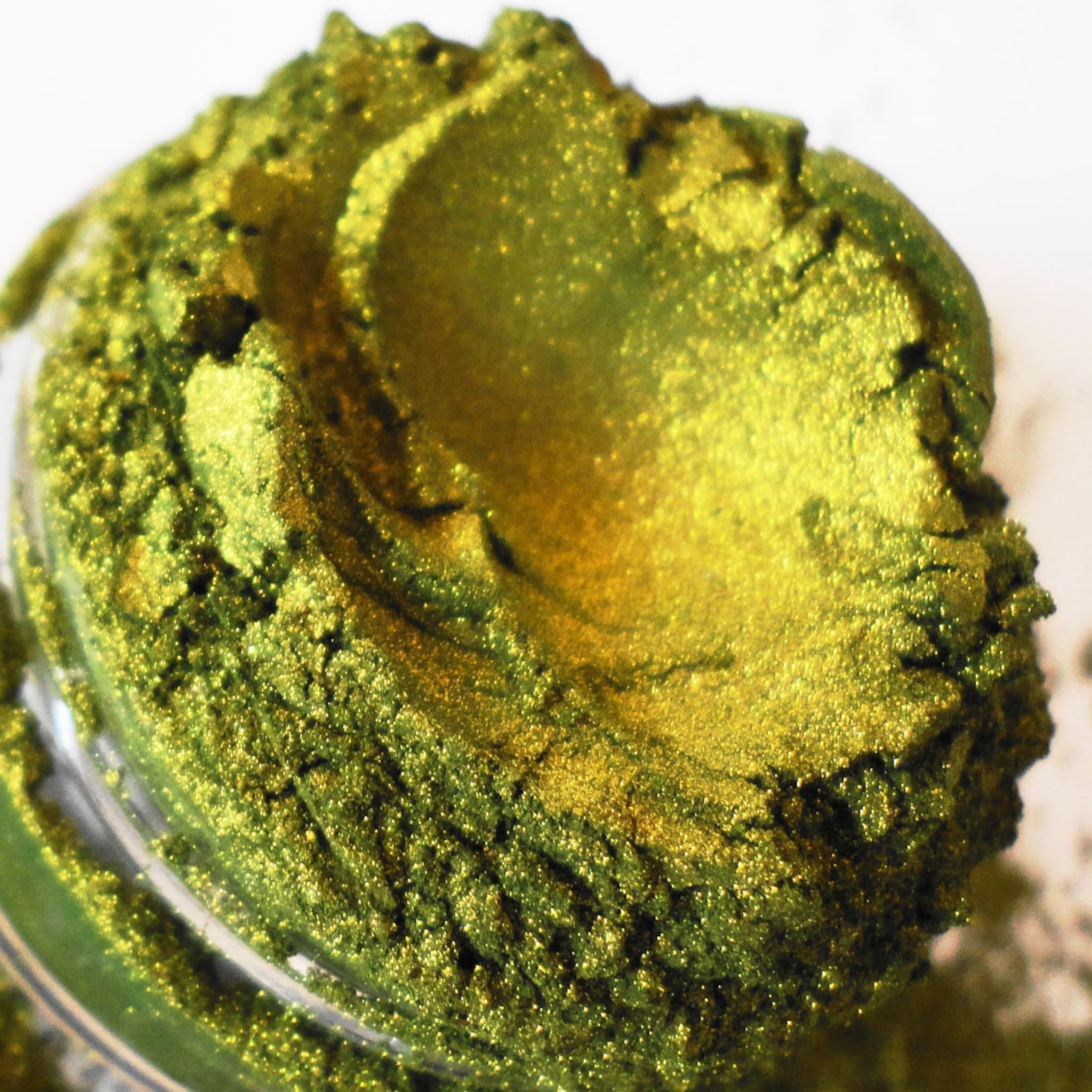 Green and gold powder with glittery texture in a clear container