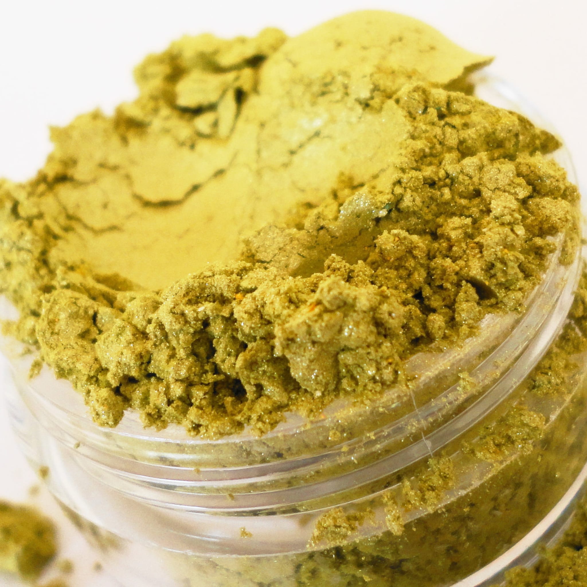 Powdered pigment in a clear plastic container, yellow-green color, granular texture, close-up view