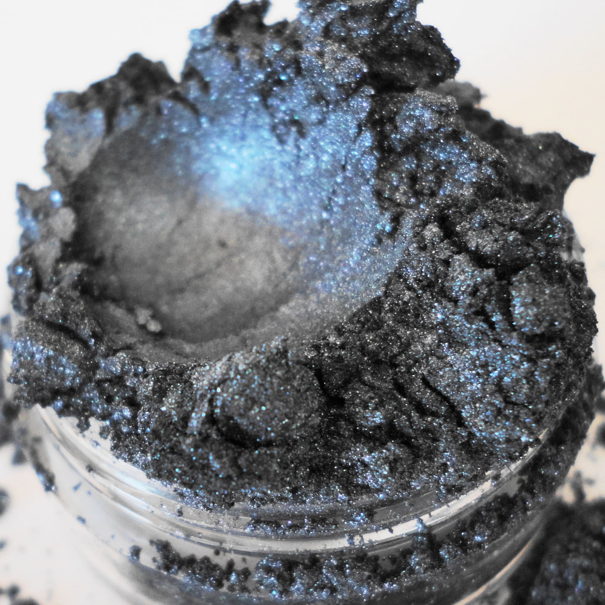 Eyeshadow powder in dark grey with blue shimmer and a glass jar container