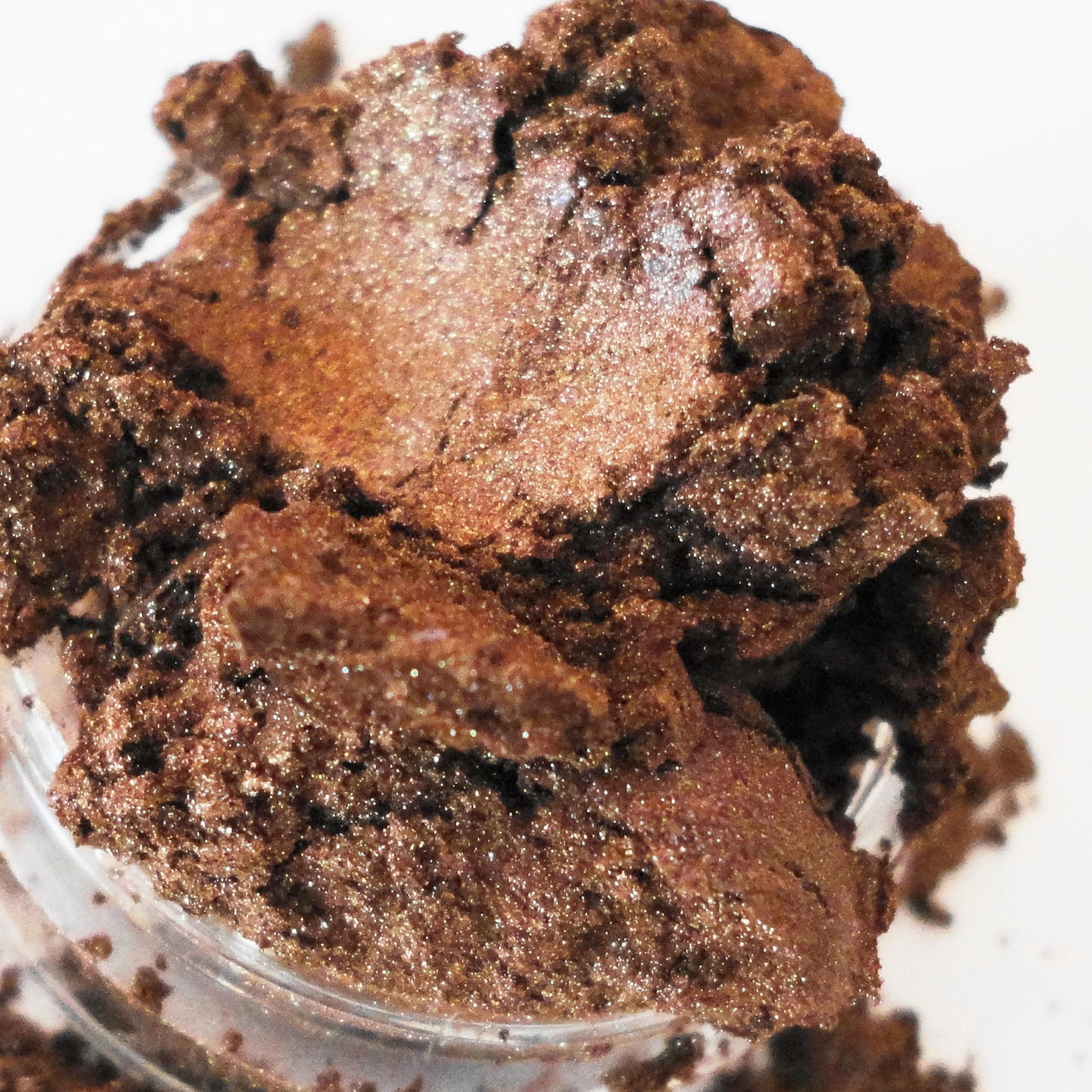 Eyeshadow powder with brown, glittery, and textured appearance in a clear container