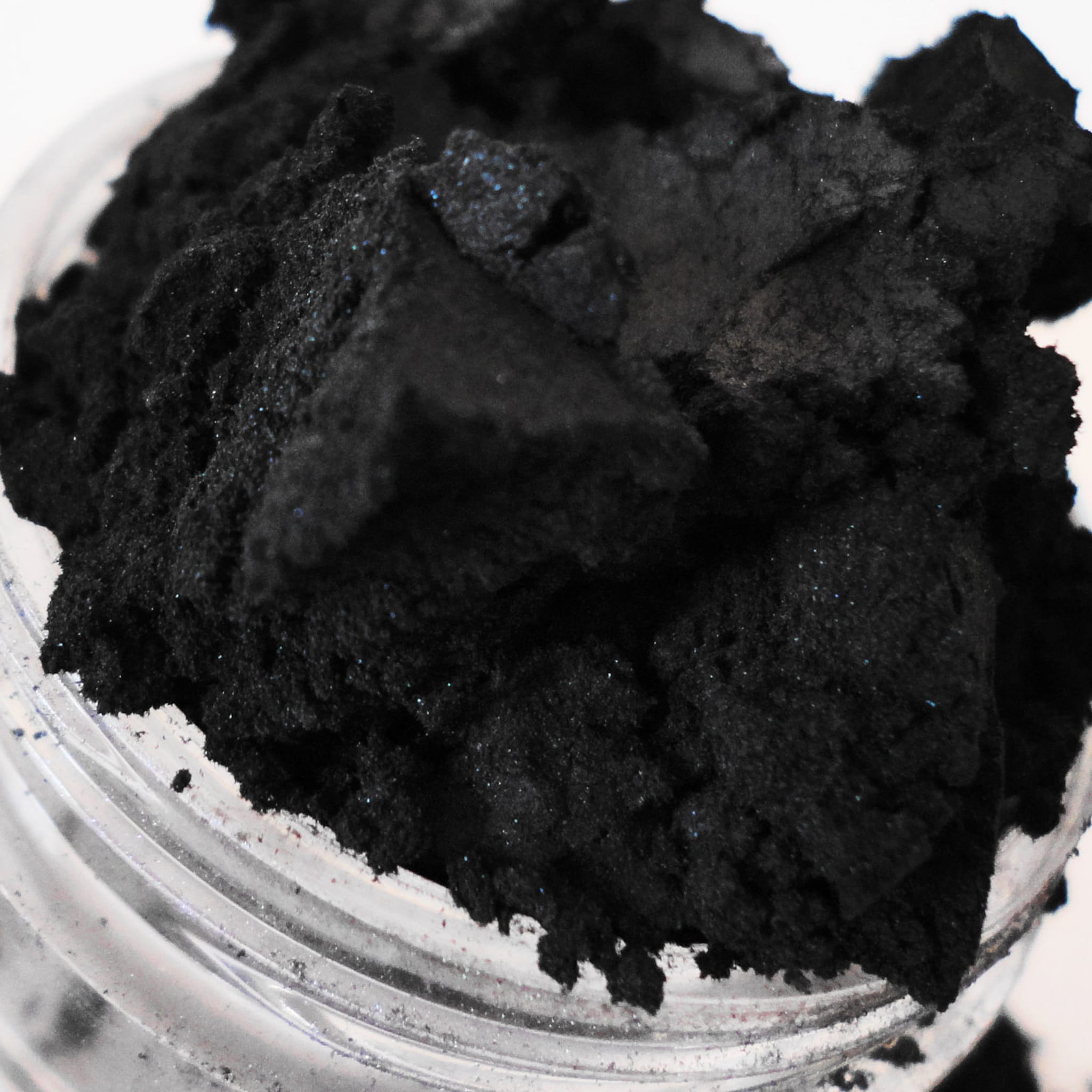 Black powder with blue sparkles in a clear jar, close-up view