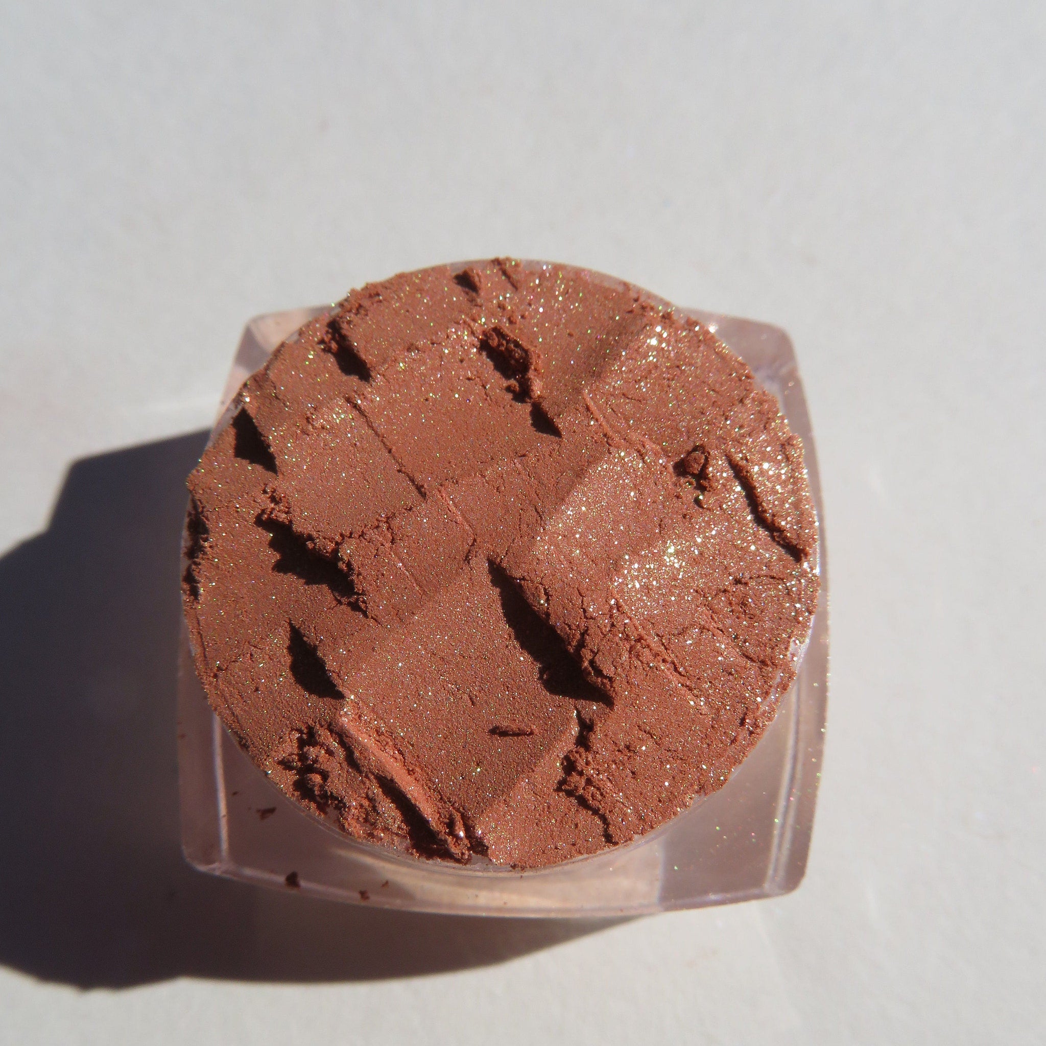 Close-up of loose brown gold mineral eyeshadow with shimmering golden flecks, showcasing fine pigment texture.