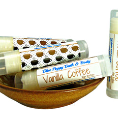 Lip balm tubes with white and brown labels, coffee cup pattern, in a wooden bowl.