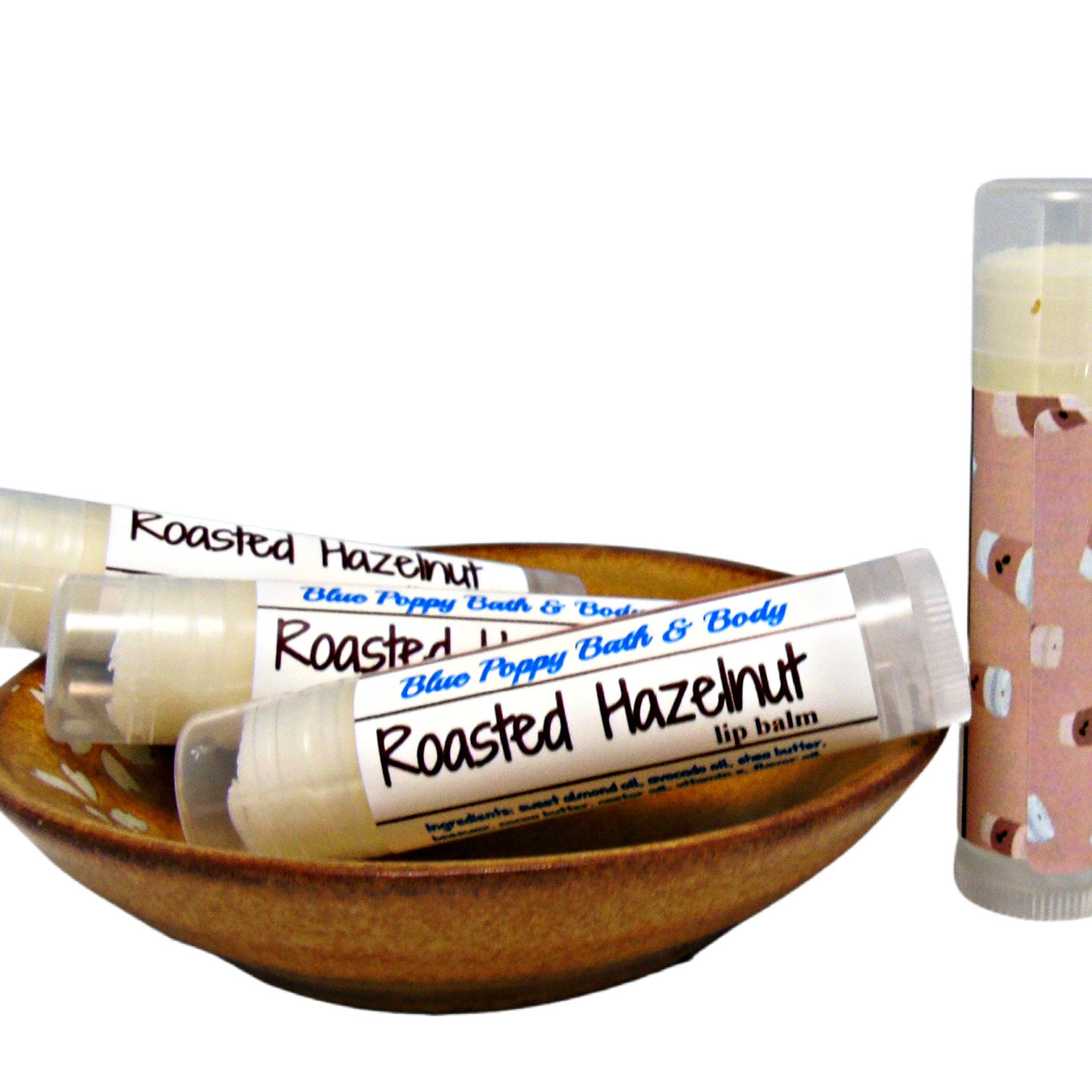Lip balm tubes with white labels, clear plastic, and "Roasted Hazelnut" text, in a brown bowl.