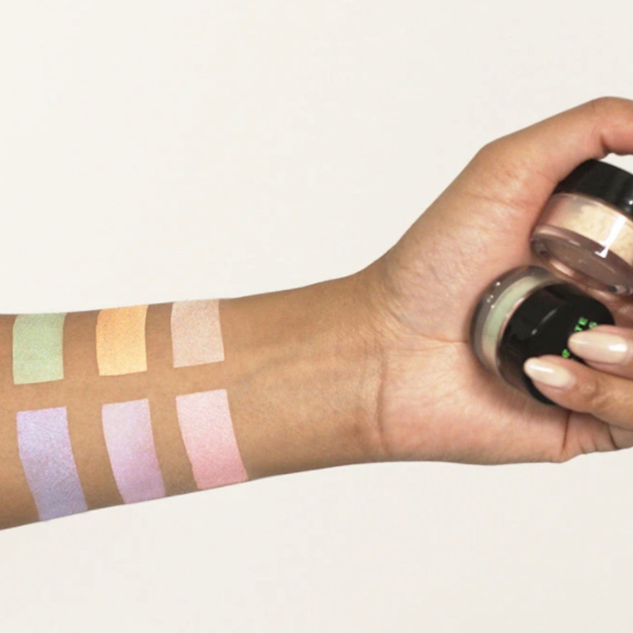 Powder swatches with green, yellow, pink, and purple shades on arm with jars