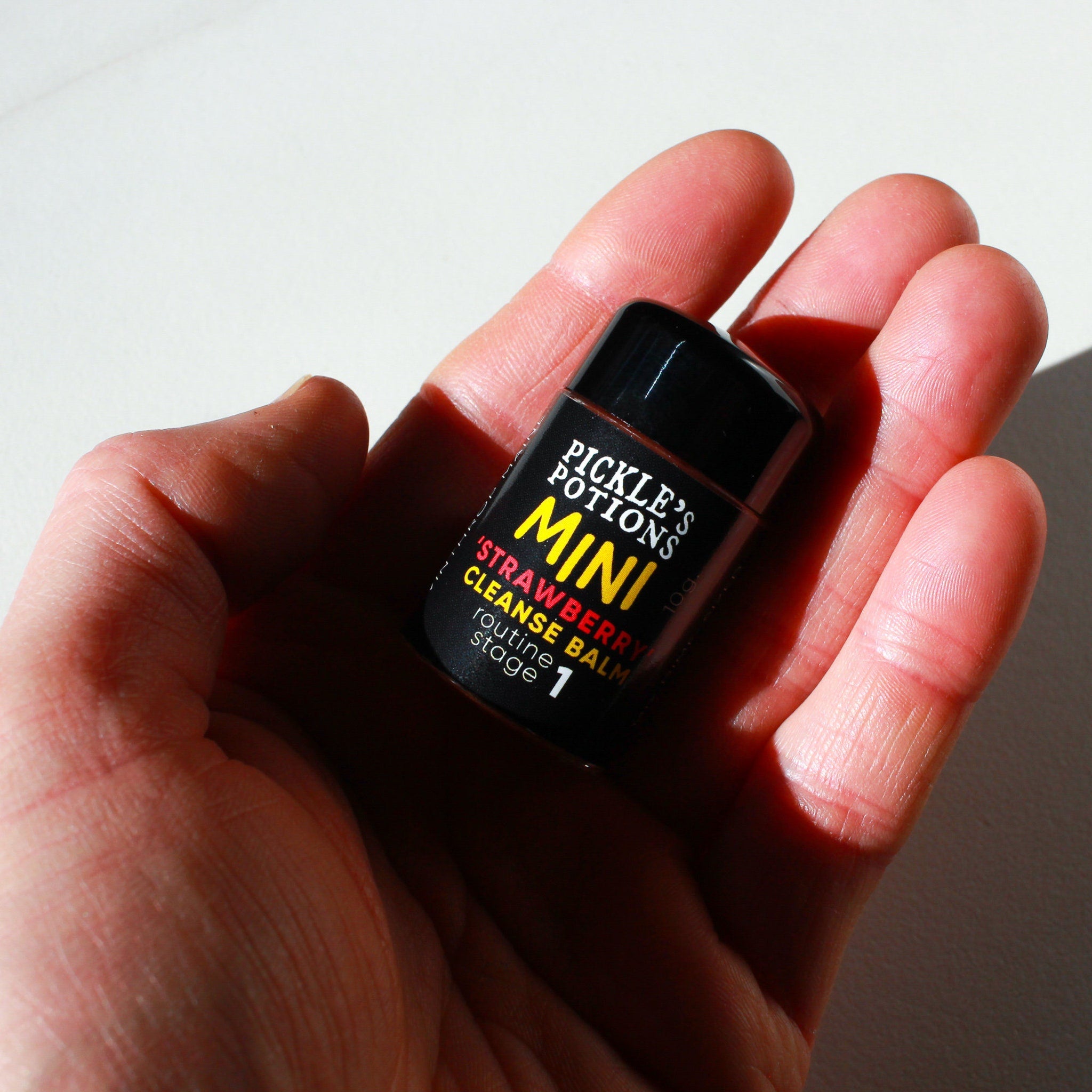 Mini cleanse balm in black bottle with yellow and red text, held in hand