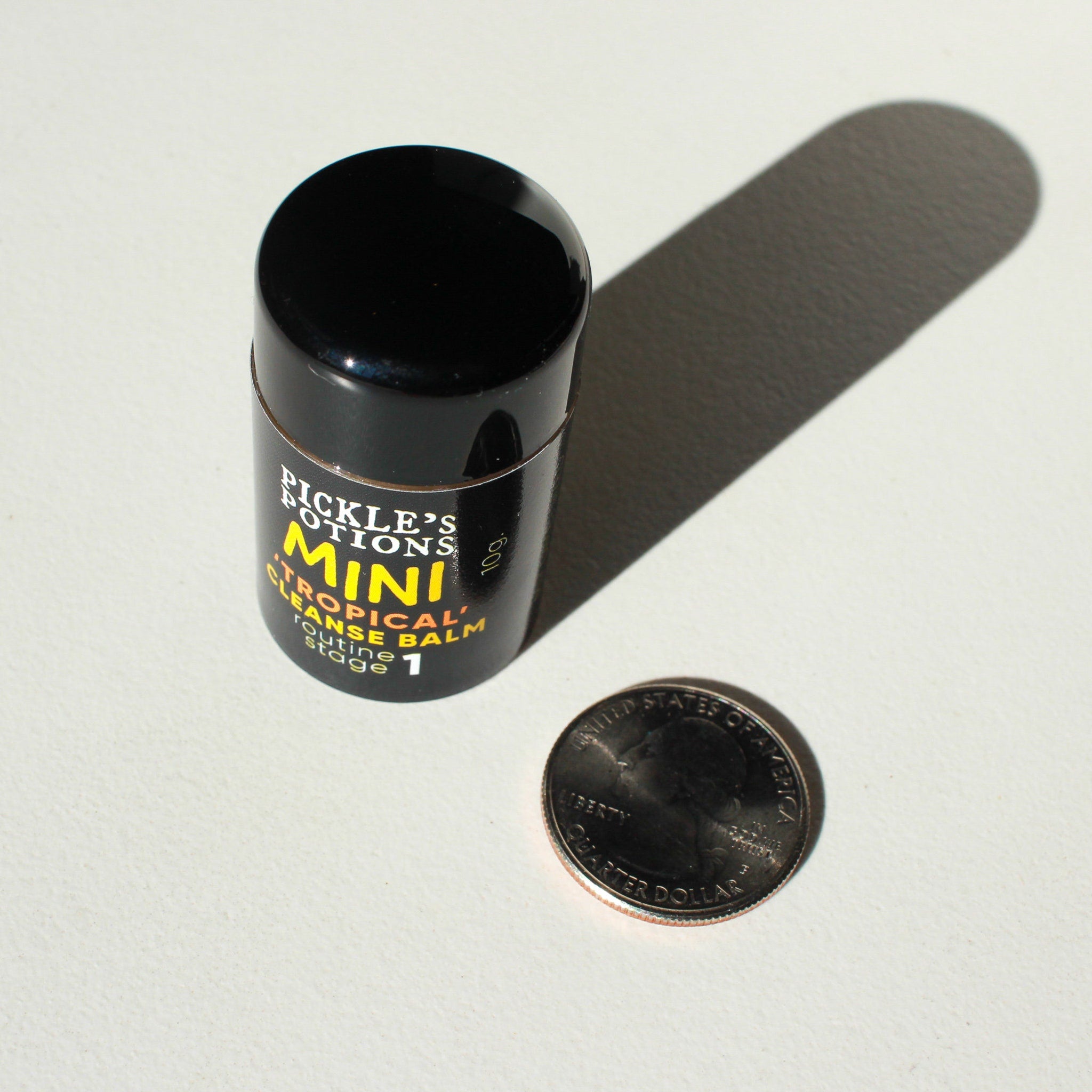 Mini cleanse balm in black cylindrical container with yellow text, next to quarter coin