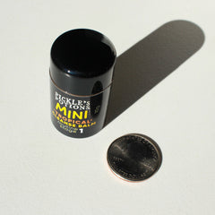 Mini cleanse balm in black cylindrical container with yellow text, next to quarter coin