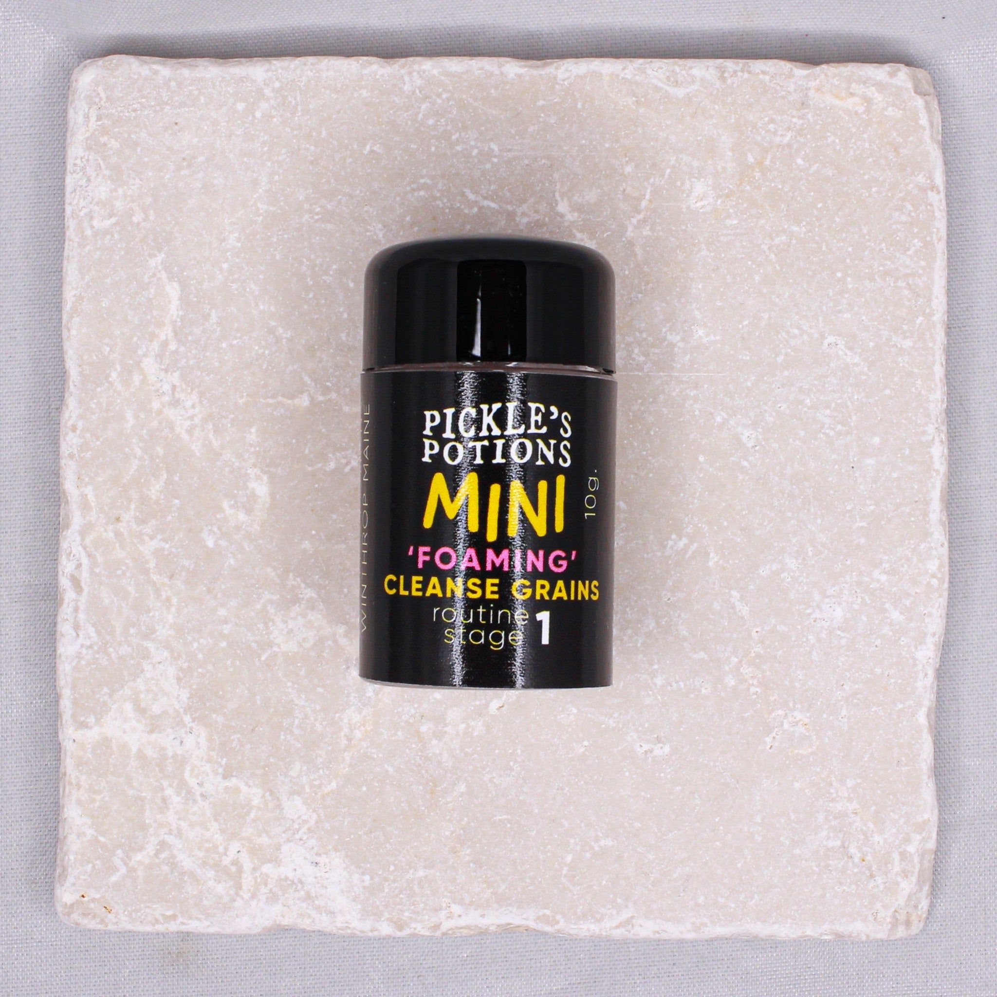 Mini foaming cleanse grains in a black container with yellow text on a stone tile background