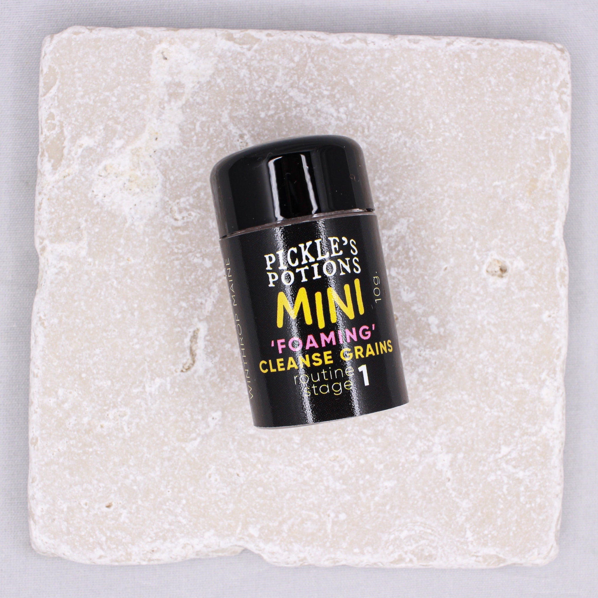 Mini Foaming Cleanser black bottle with yellow text on light stone surface