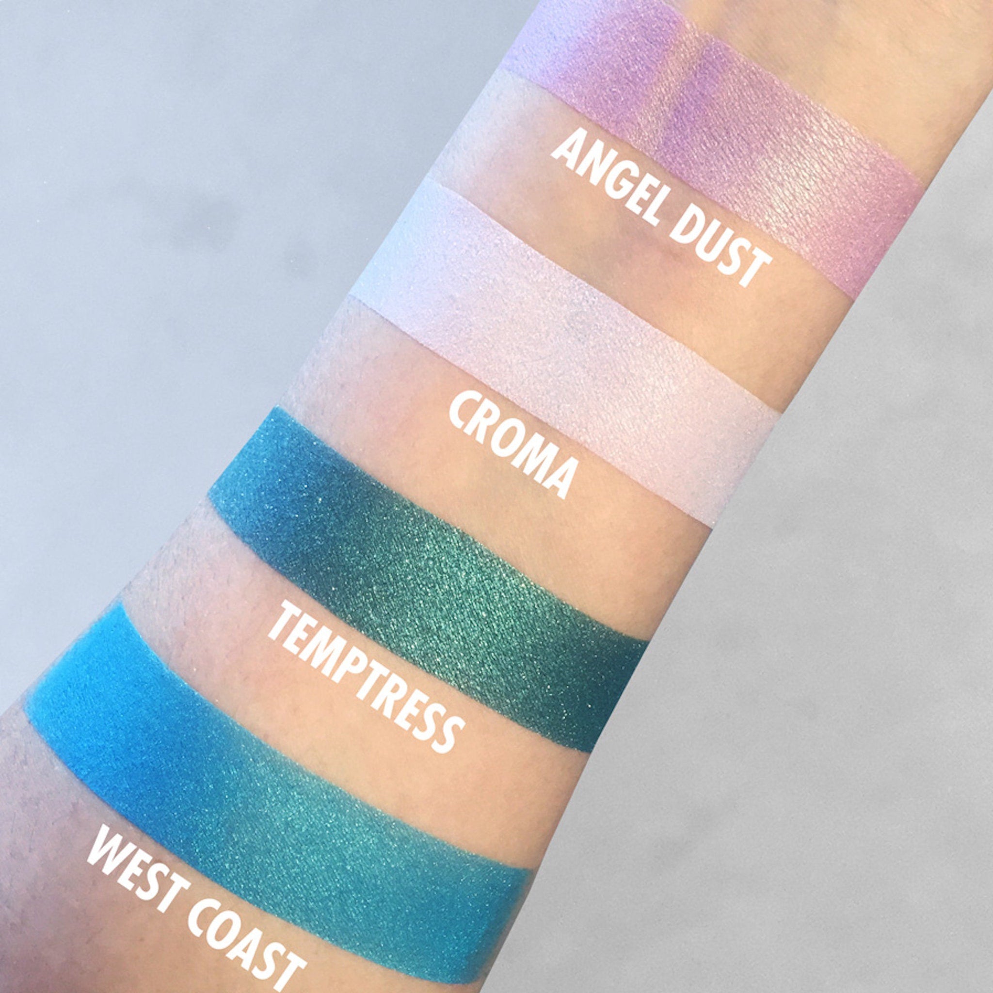 Eyeshadow swatches, various colors including blue, green, and pink, with white text labels on arm