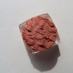 Hand applying burnt orange matte mineral eyeshadow with a fluffy brush, showcasing pigment intensity