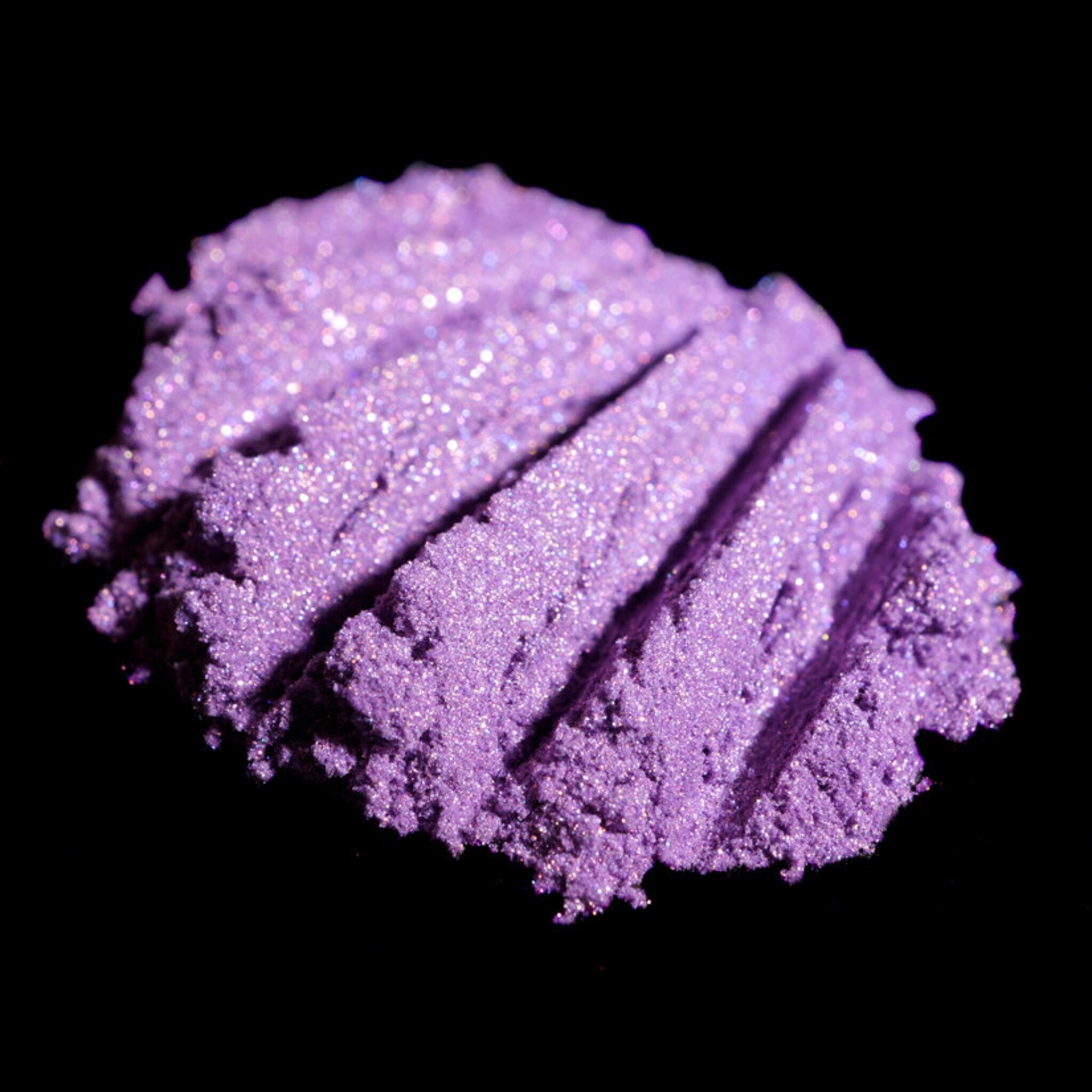 Purple eyeshadow powder with glitter and textured surface on black background