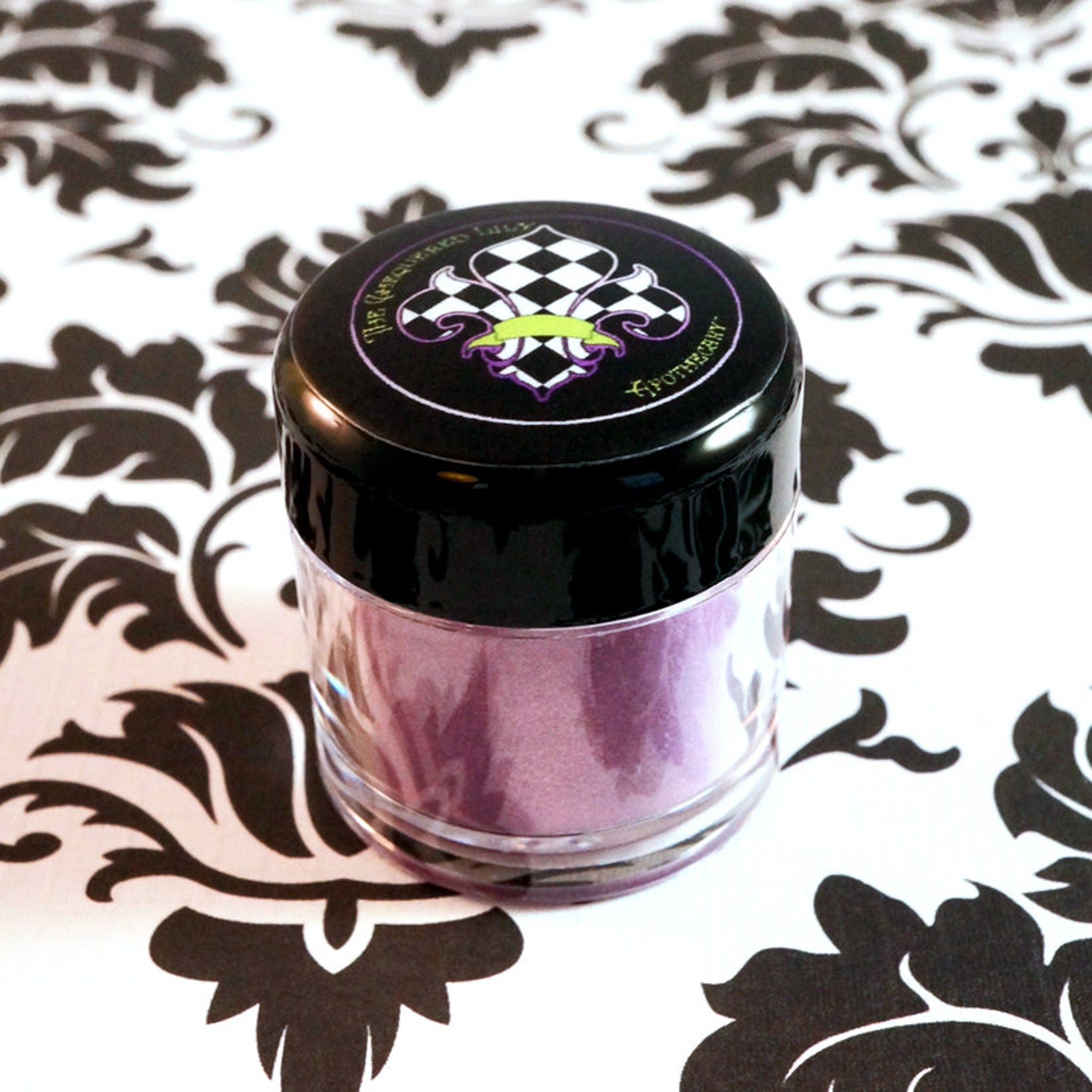 Cosmetic jar with black lid, clear container, and purple powder, on floral pattern background