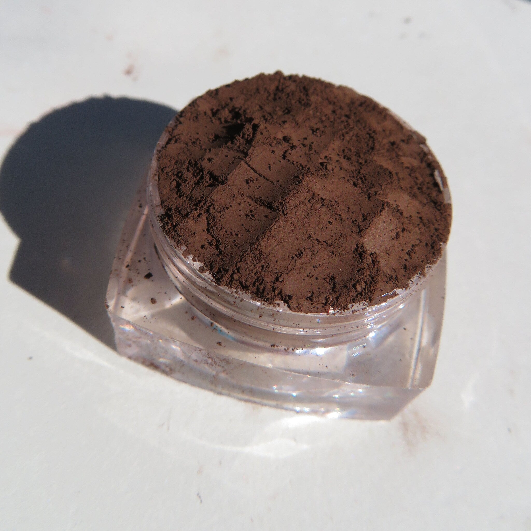 Side view of matte brown mineral eye shadow in loose powder form with vegan label visible