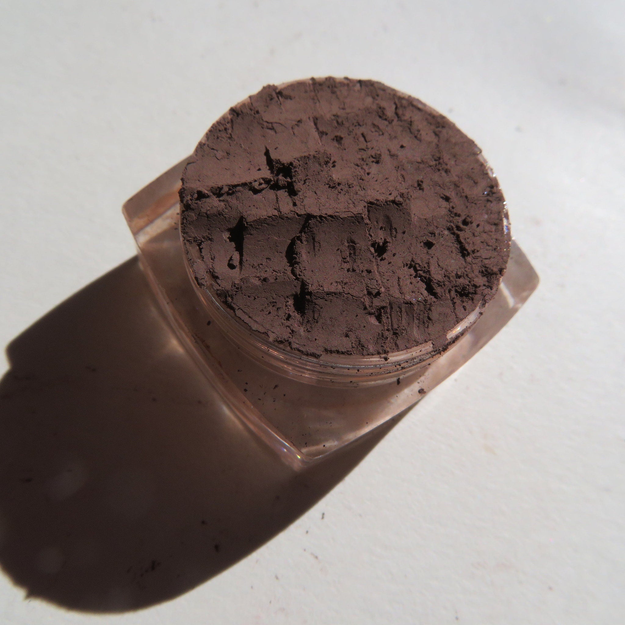 Close-up of loose dark matte brown mineral eye shadow powder in open jar with fine texture