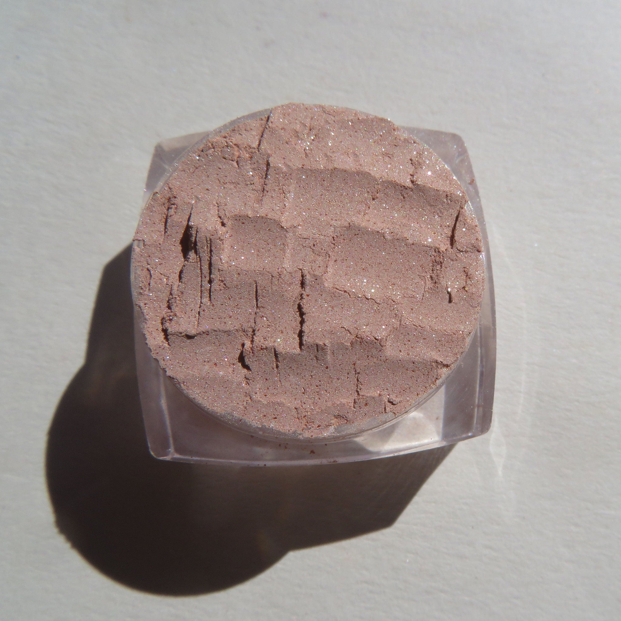 Hand applying shimmering champagne-beige loose mineral eyeshadow with fingertip for a frosty golden glow